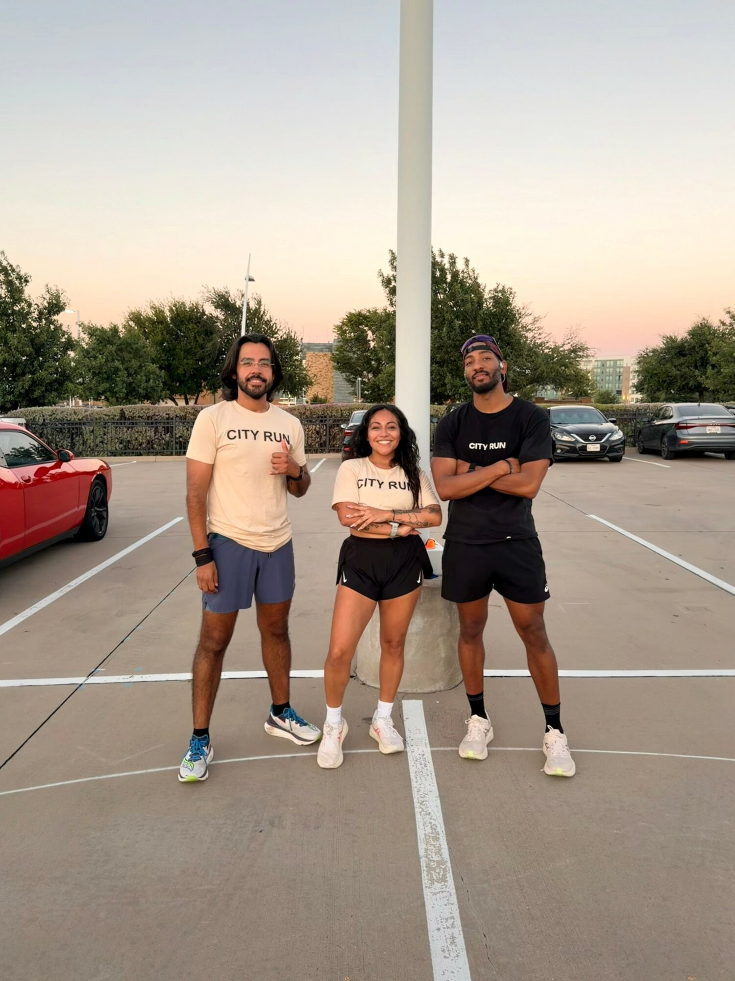 Three people standing in a parking lot, with cars and trees in the background, under a clear sky.