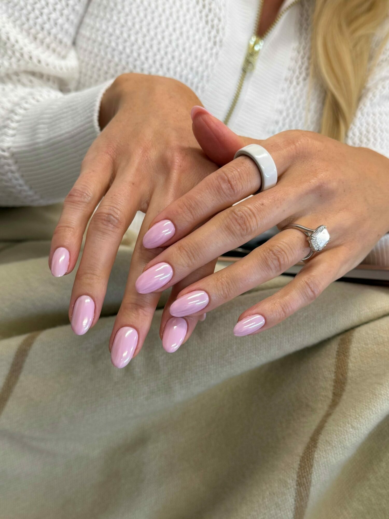 Close-up of hands with manicured nails and rings, resting on a beige fabric surface.