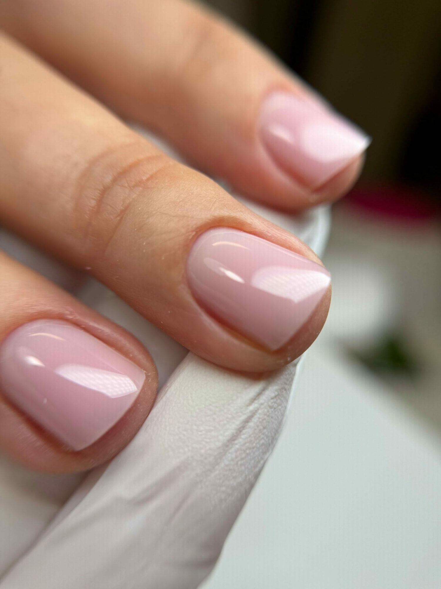 Close-up of three fingers with well-manicured, shiny, light pink nails holding a white paper or tissue.