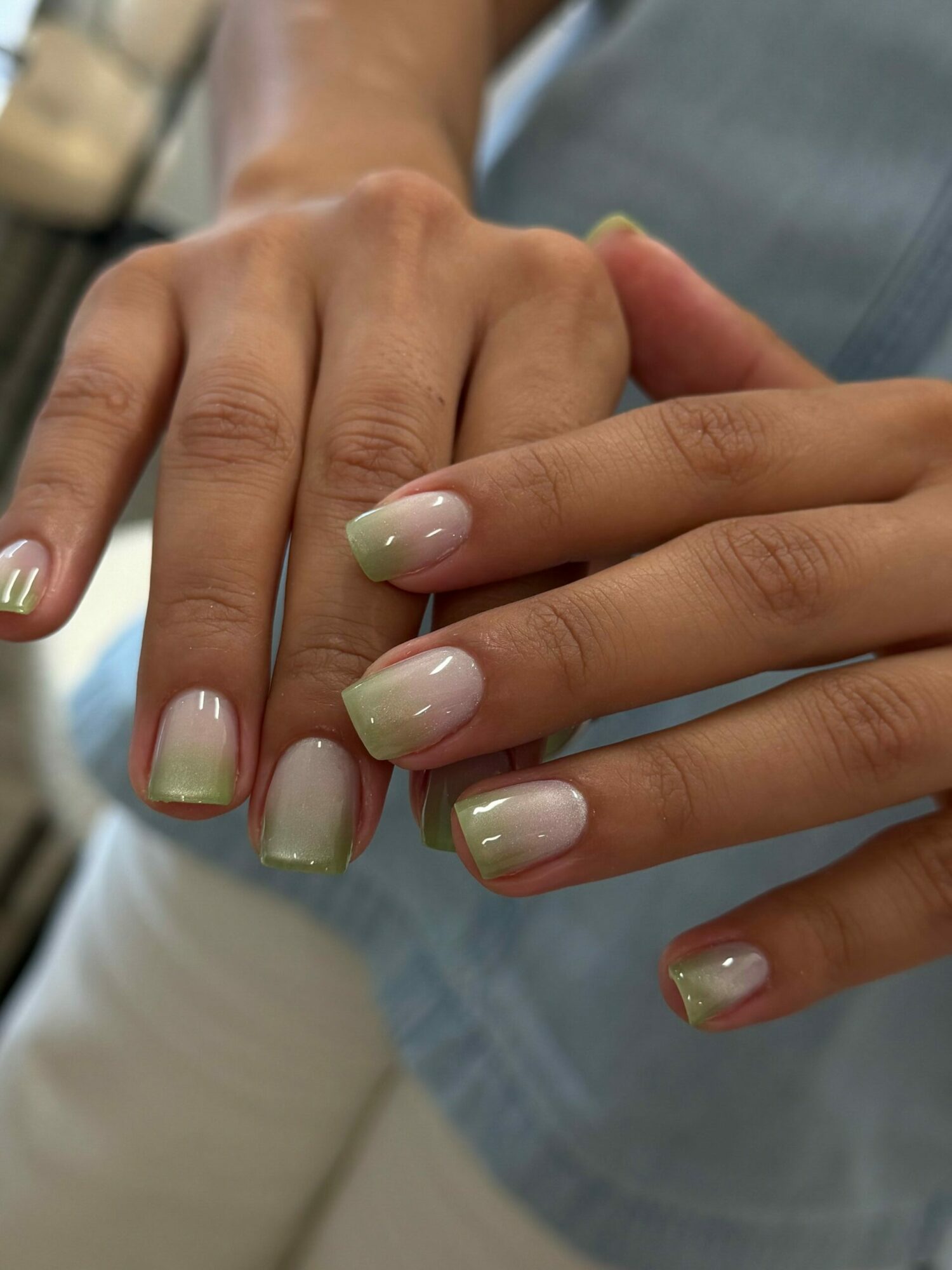 Person's hands with neatly manicured nails painted in light green with gold tips, resting on a surface.