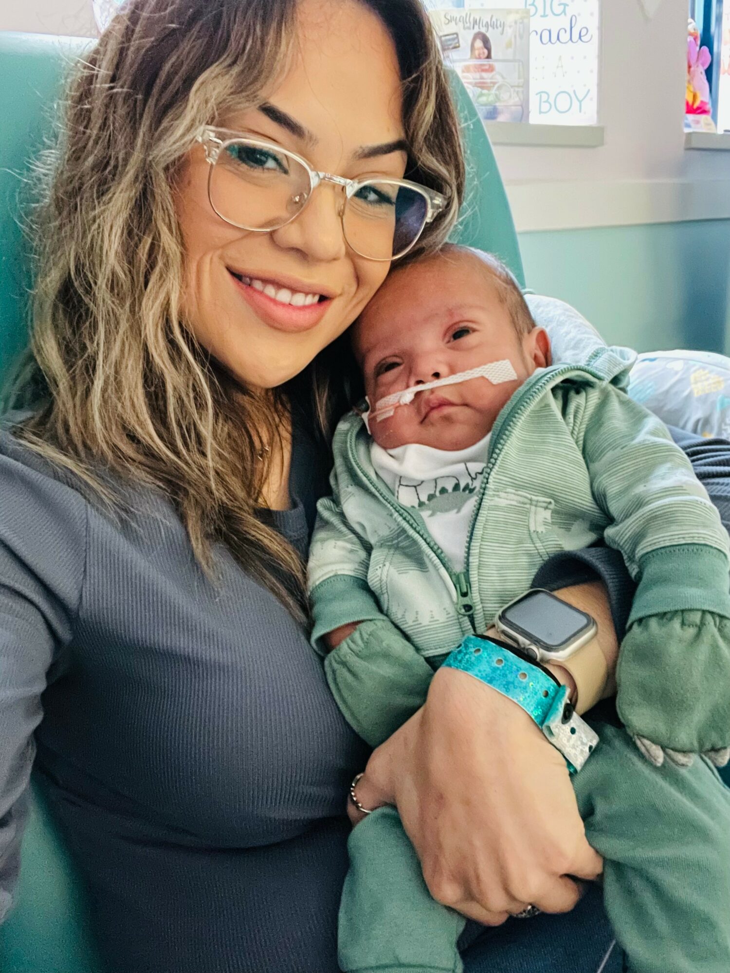 Woman holding a baby with a nasal cannula, both smiling, in a hospital room.
