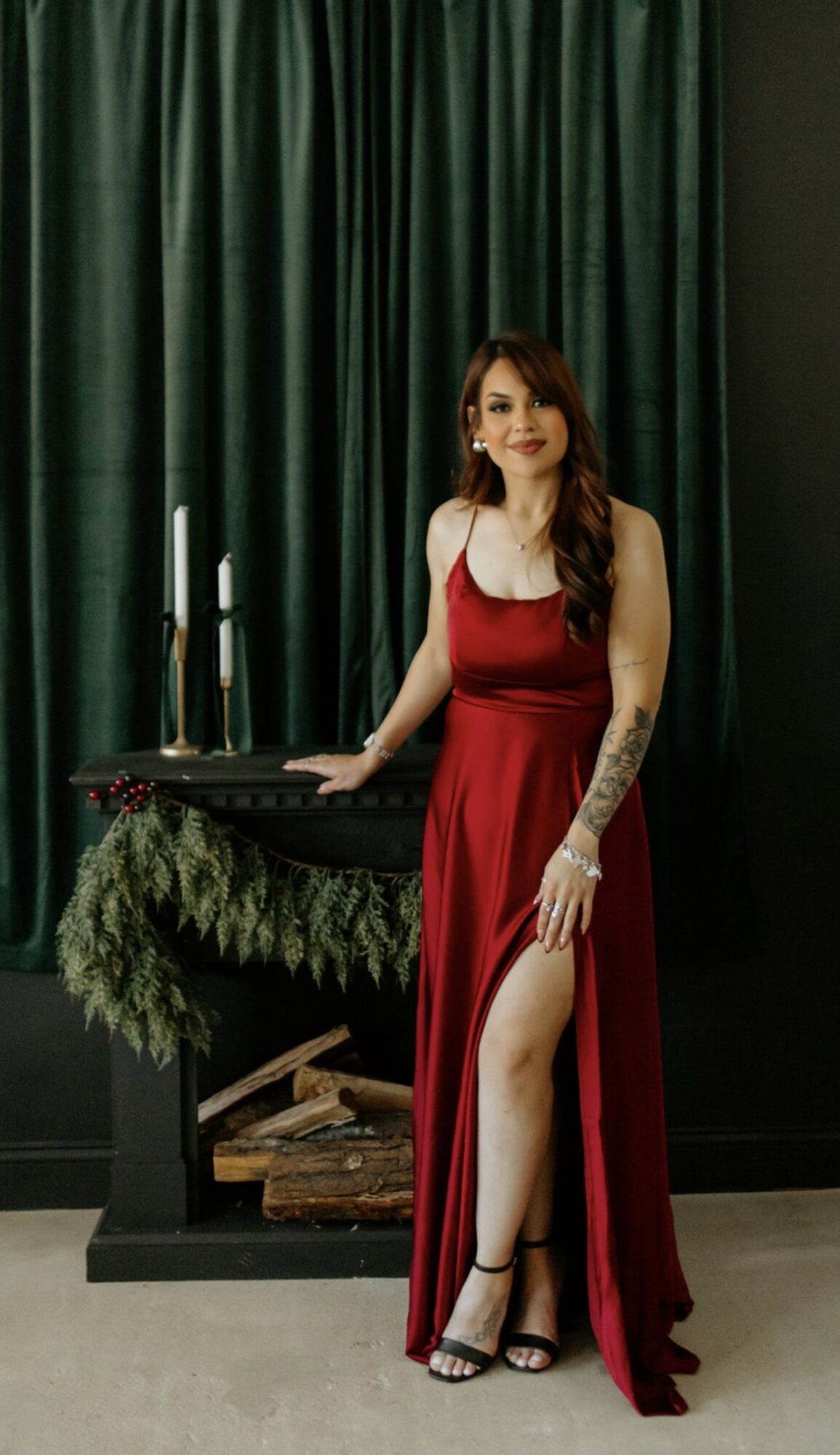 Woman in red dress with tattoo standing next to a keyboard, green curtain background, holding a microphone, smiling.