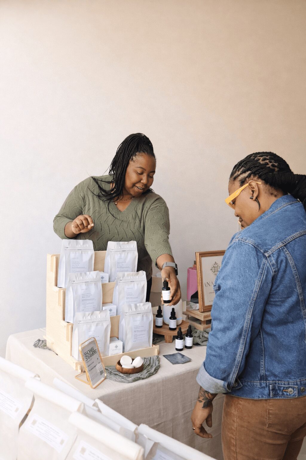 Two women at a table with skincare products, one smiling and the other looking at the products.