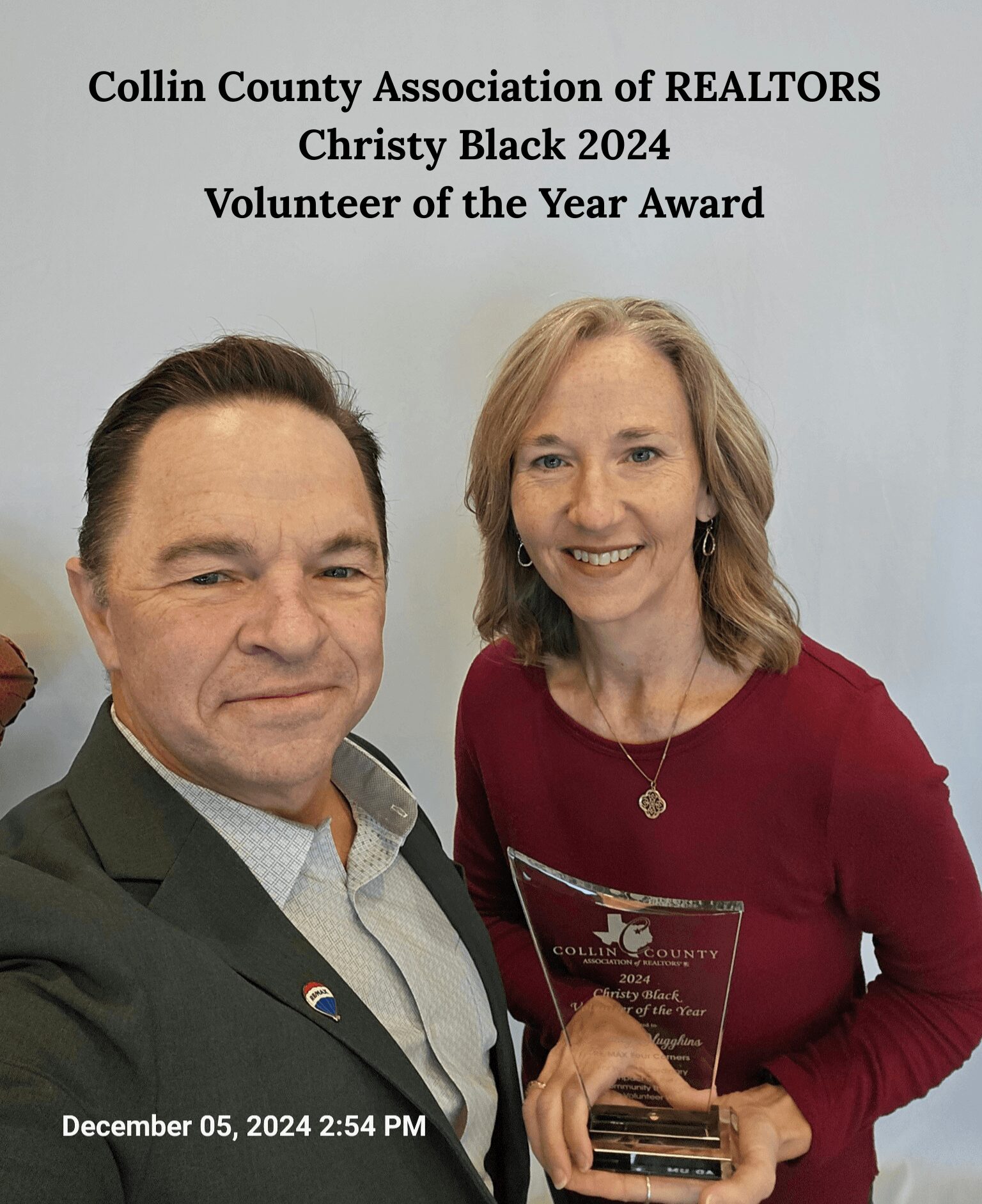 Two people, a man and a woman, smiling at an award ceremony, woman holding a plaque, background with text about an award.