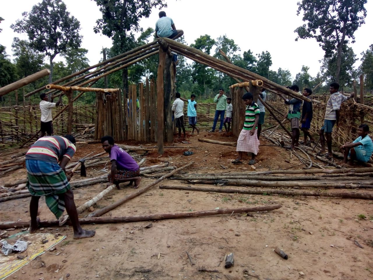 Group of people building a wooden structure outdoors with trees in the background.