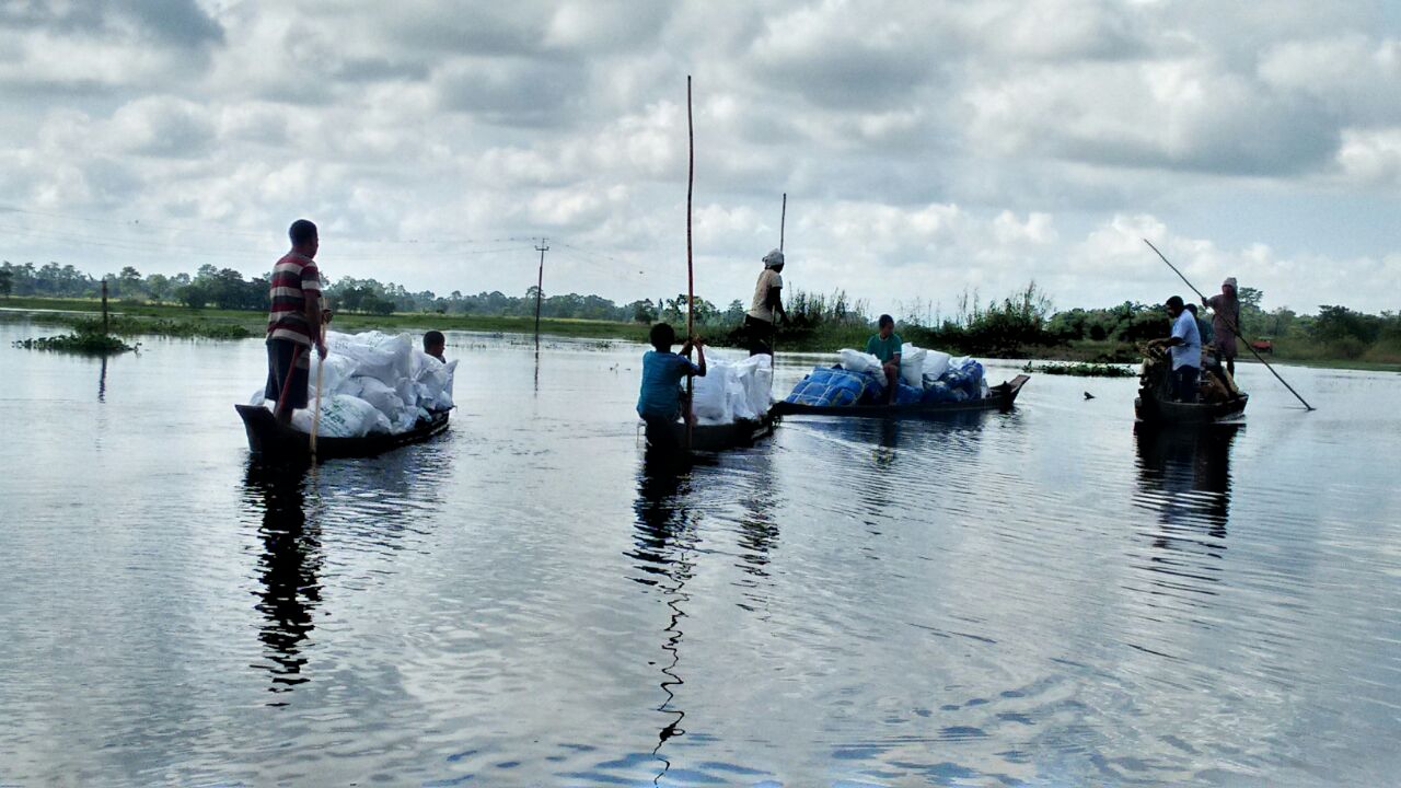 Three boats with people on water, cloudy sky, and distant shoreline, with reflections in the water.