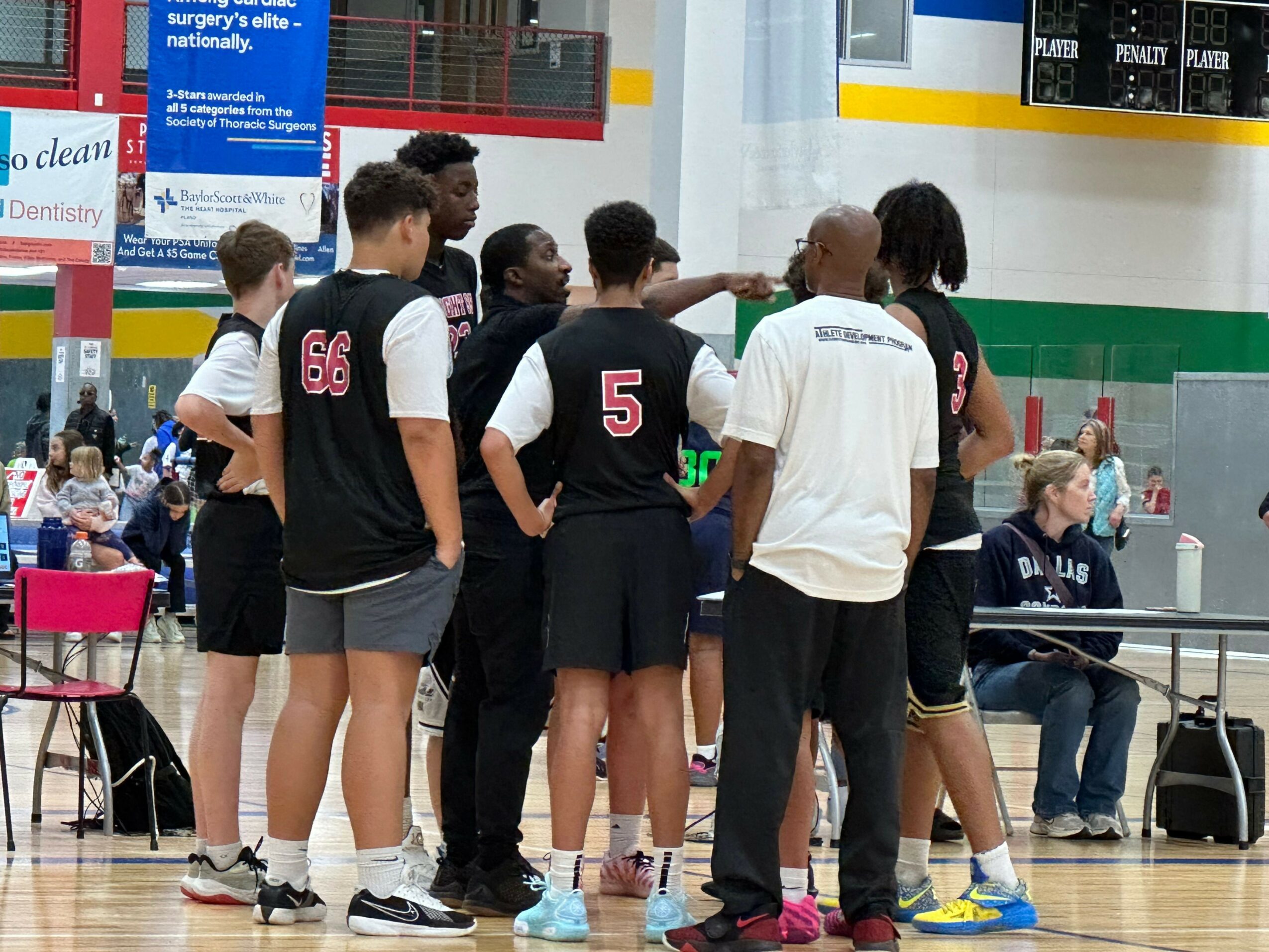 Group of people standing in a line indoors, some wearing sportswear, with a colorful wall and signs in the background.