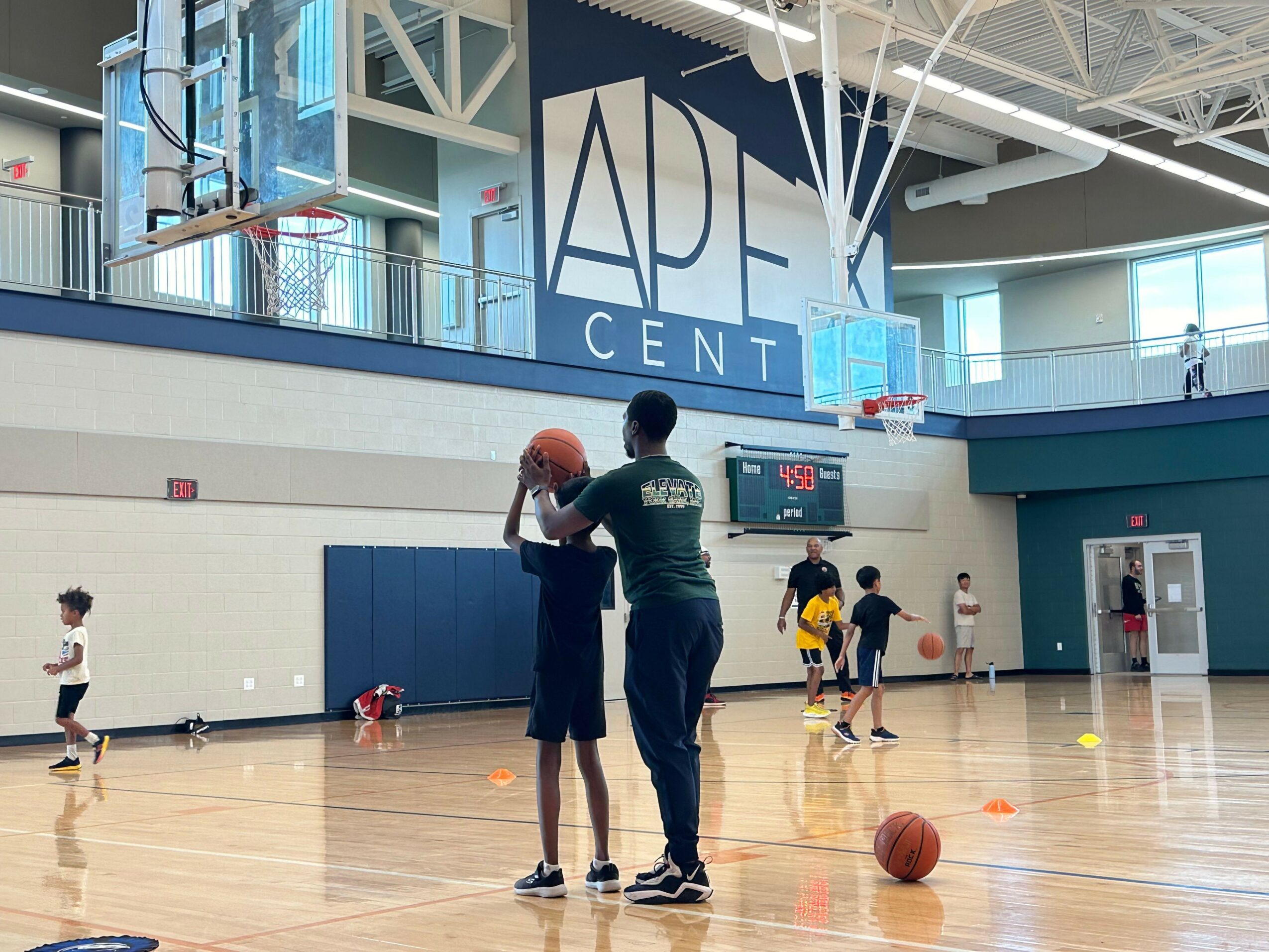 People playing basketball on an indoor court with a large sign reading 'CADE CENTER' on the wall, some holding basketballs.