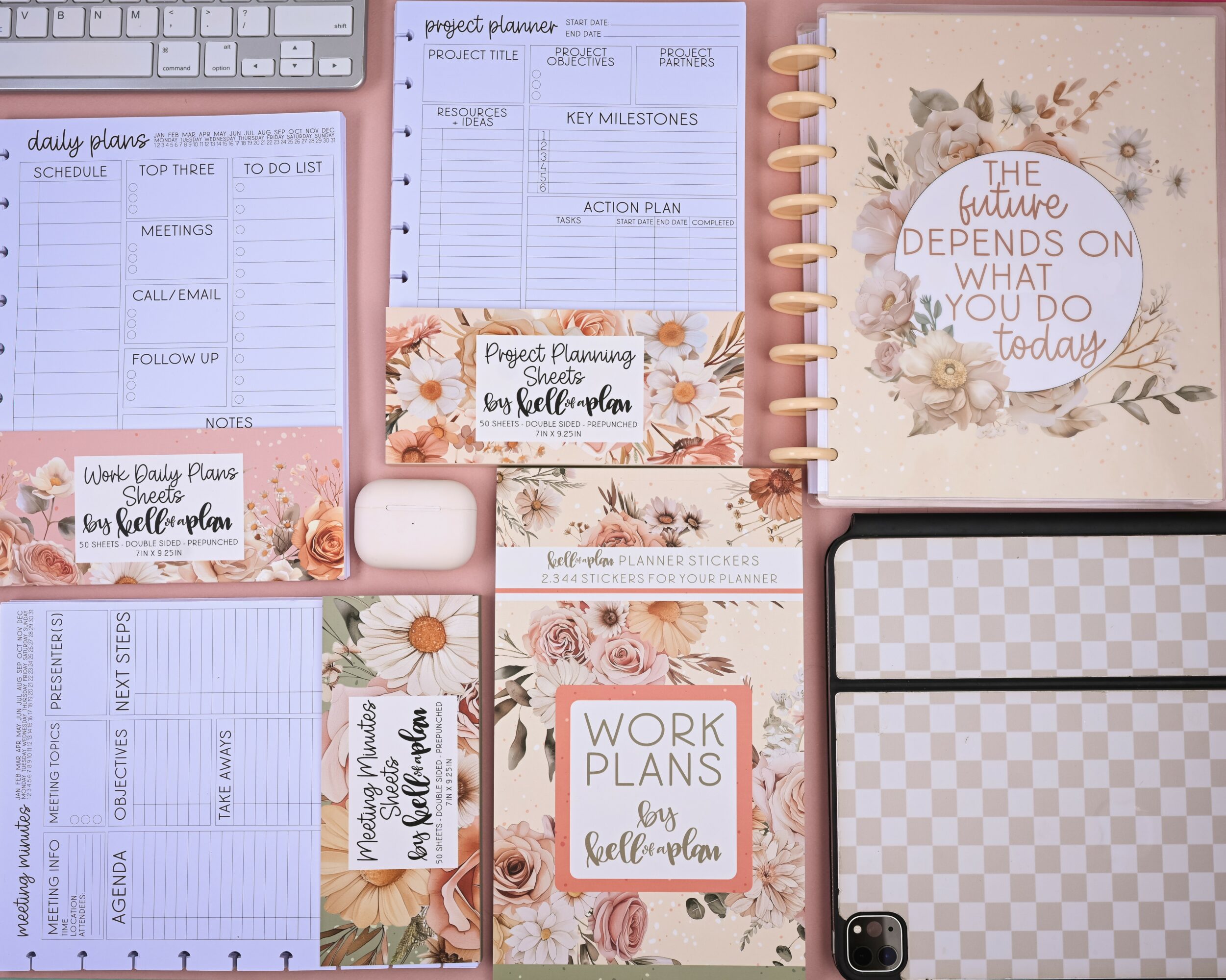 Flat lay of planners, notebooks, and accessories with floral designs and motivational quotes, arranged on a surface.