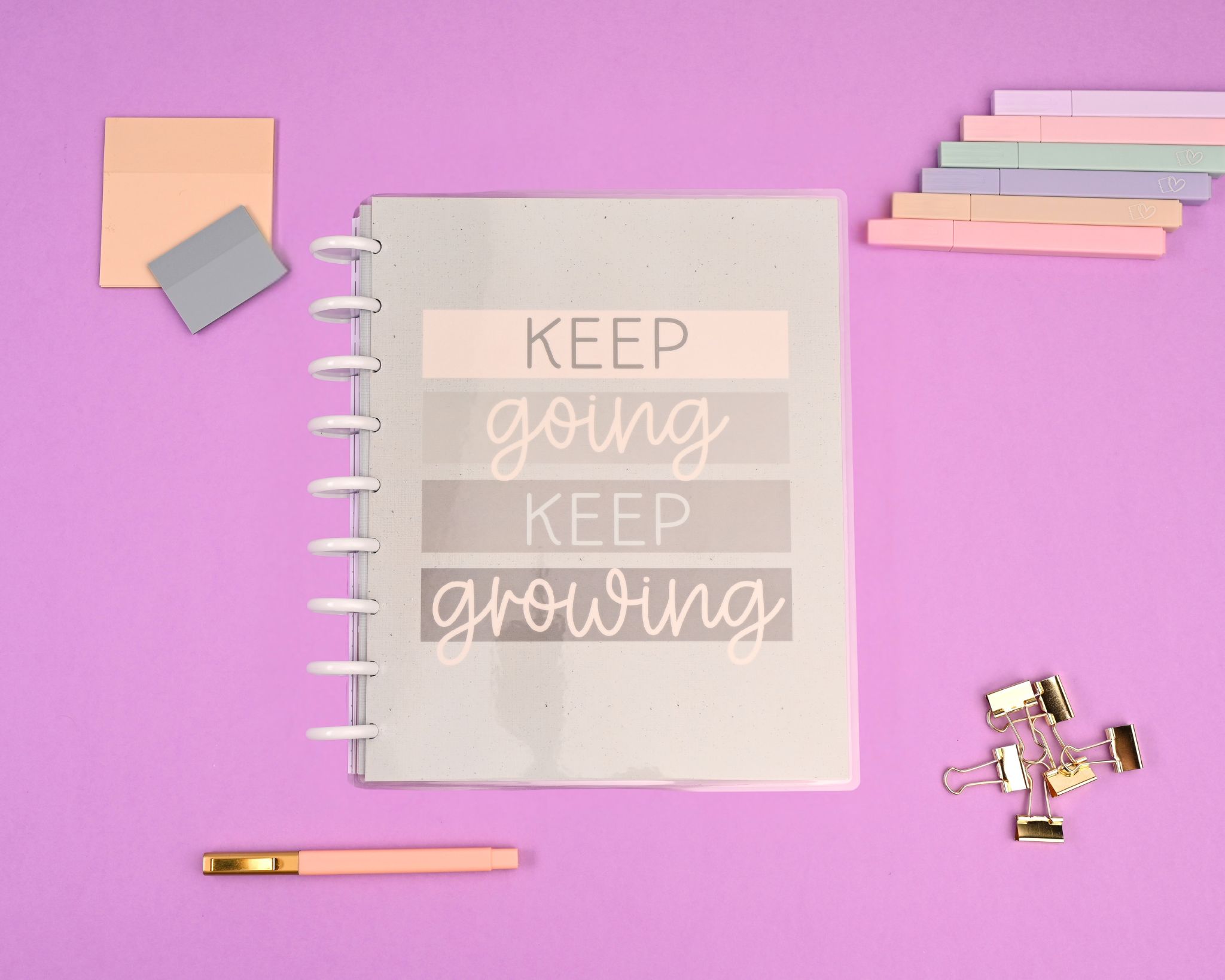 Notebook with motivational quote on a purple background, surrounded by sticky notes, paper clips, and a pen.