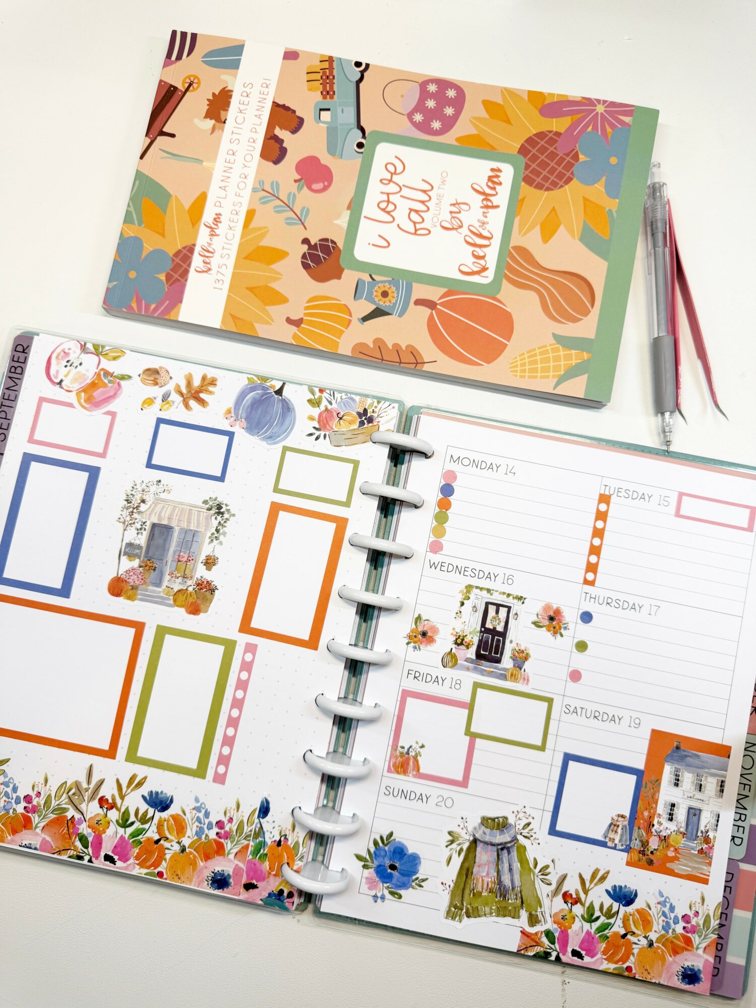 Open planner with colorful floral and decorative elements, pages showing weekly layout, and a closed floral-themed notebook on top.