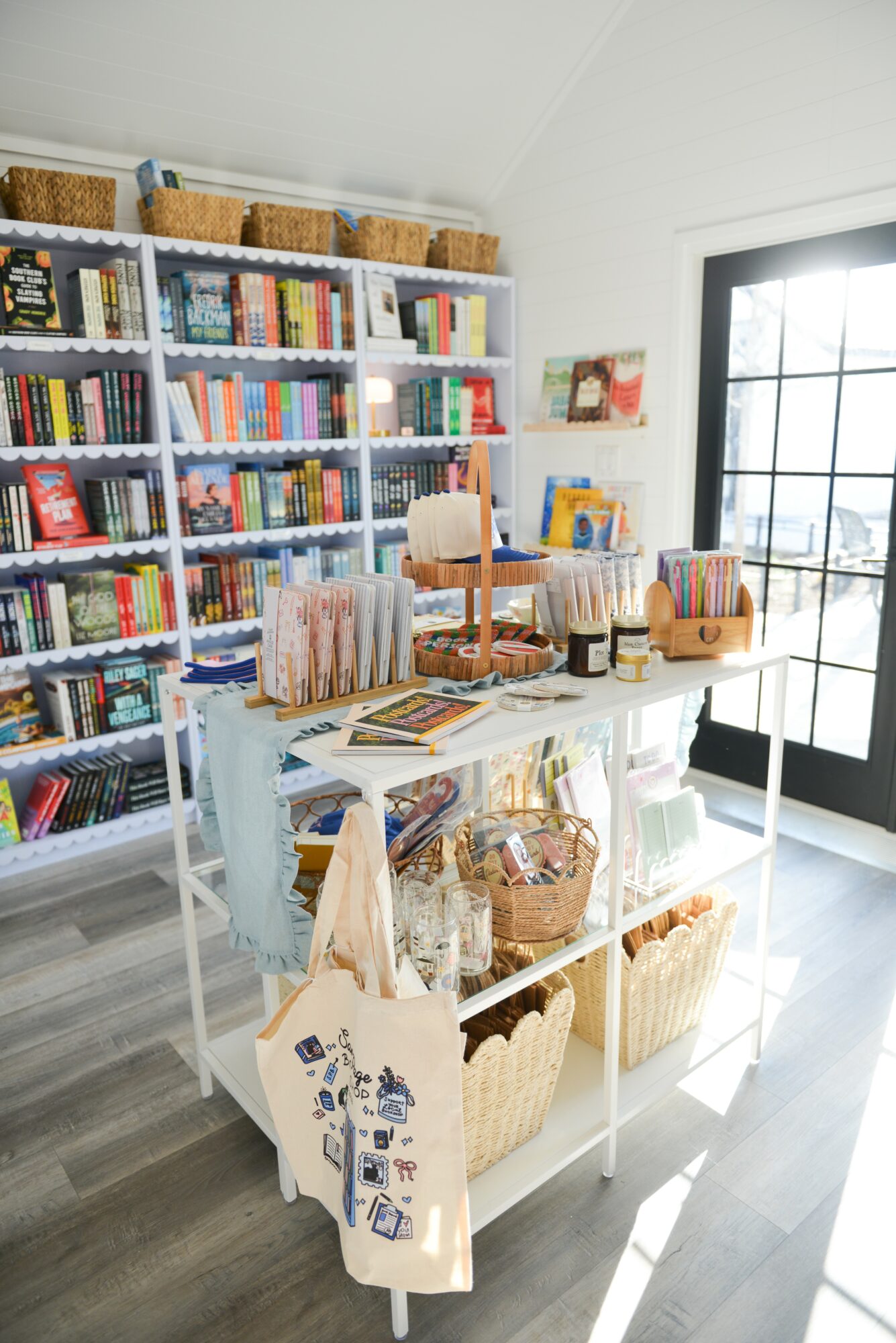 Bookshelves filled with books, a table with baskets and books, and a large window with sunlight streaming in.