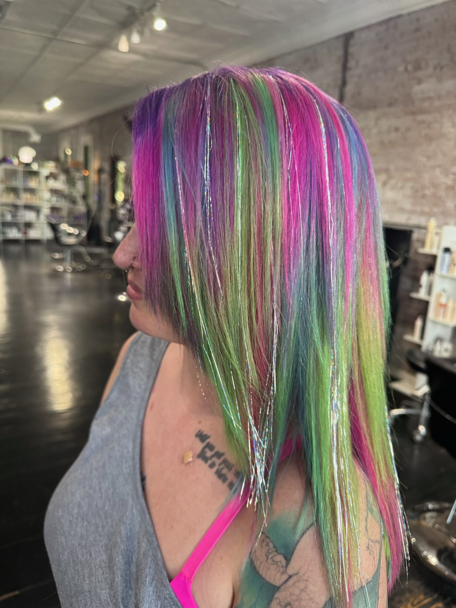 Side view of a woman with long, straight, multicolored hair in pink, green, purple, and blonde shades, indoors.