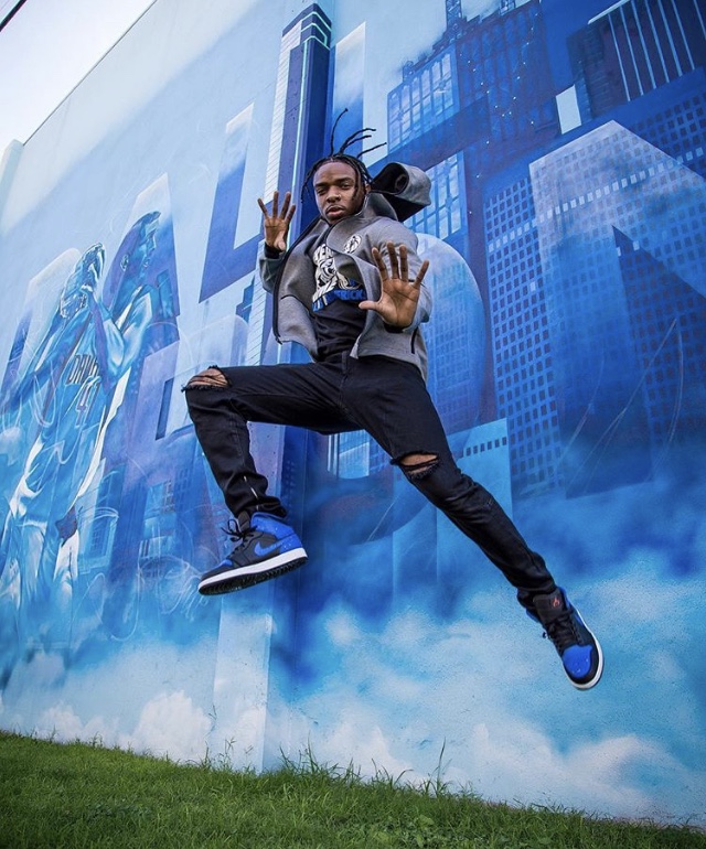 Person jumping in front of a blue cityscape mural, with one hand raised and legs spread apart.