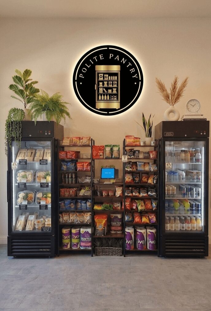 Display of snacks and beverages with a circular sign reading 'POLITE PANTRY' above, flanked by plants on both sides.