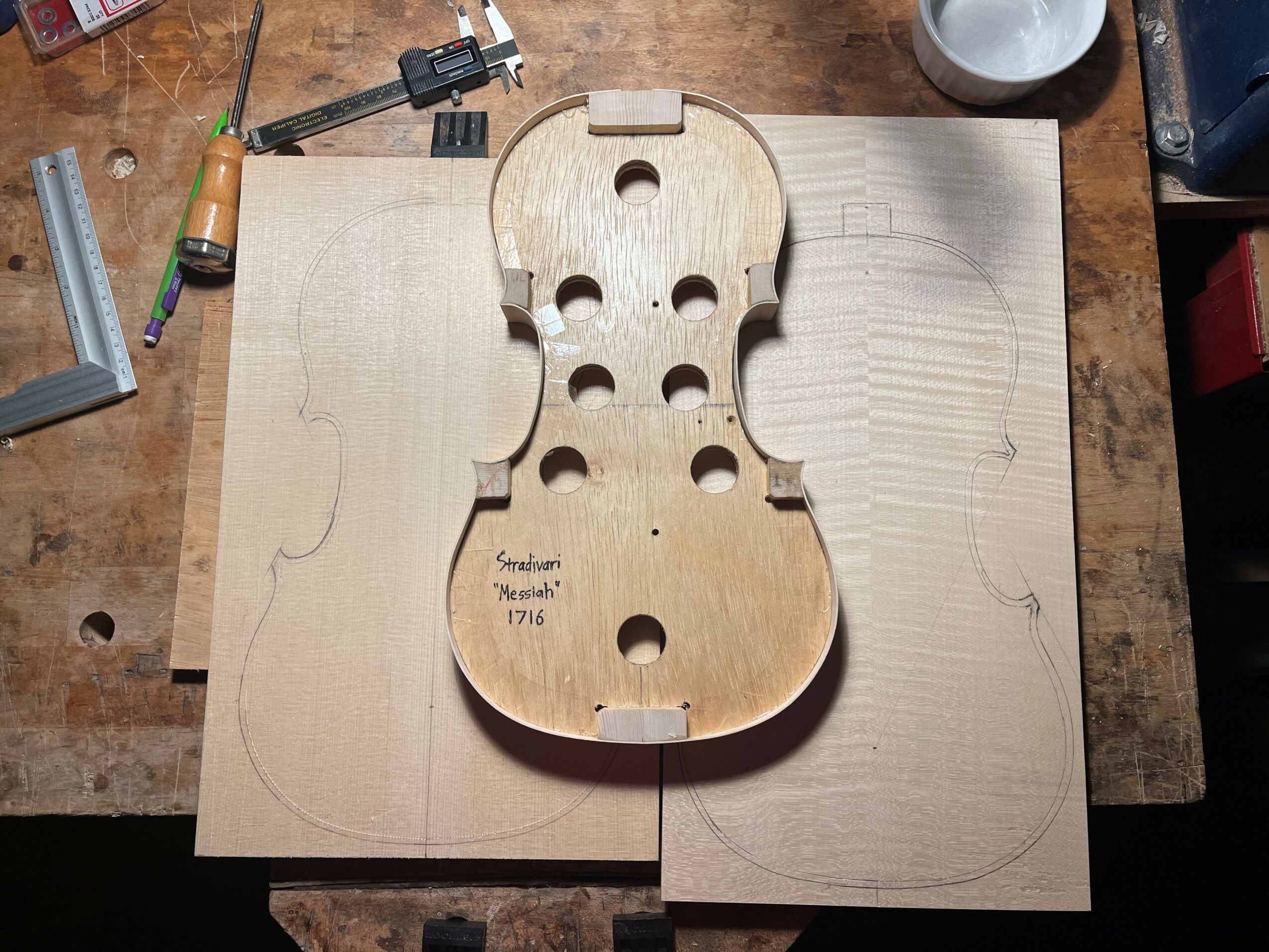 Wooden guitar body template on a workbench with tools and wood pieces around.