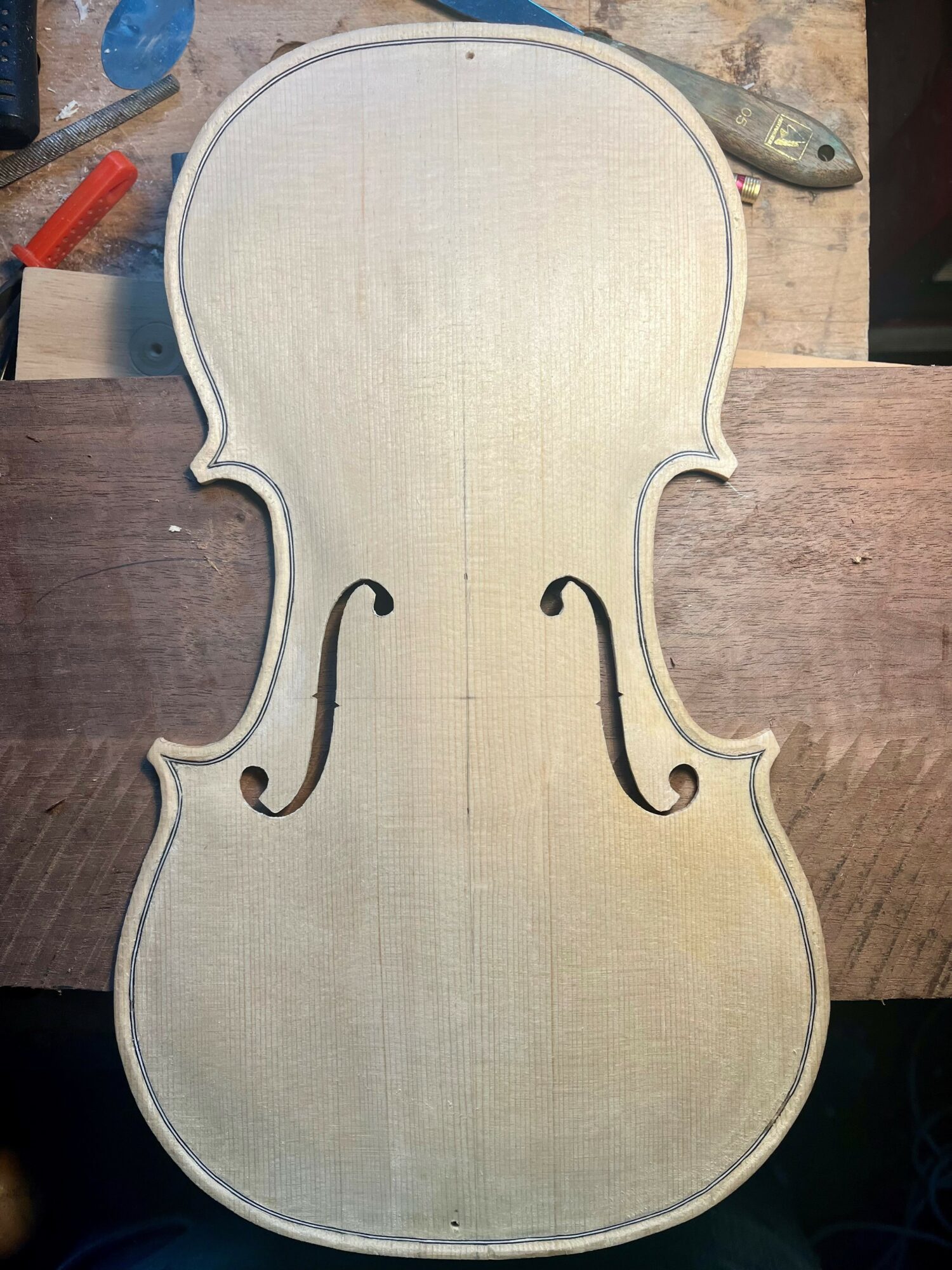 Unfinished violin-shaped wooden piece with a light-colored surface and dark edges, on a workbench.