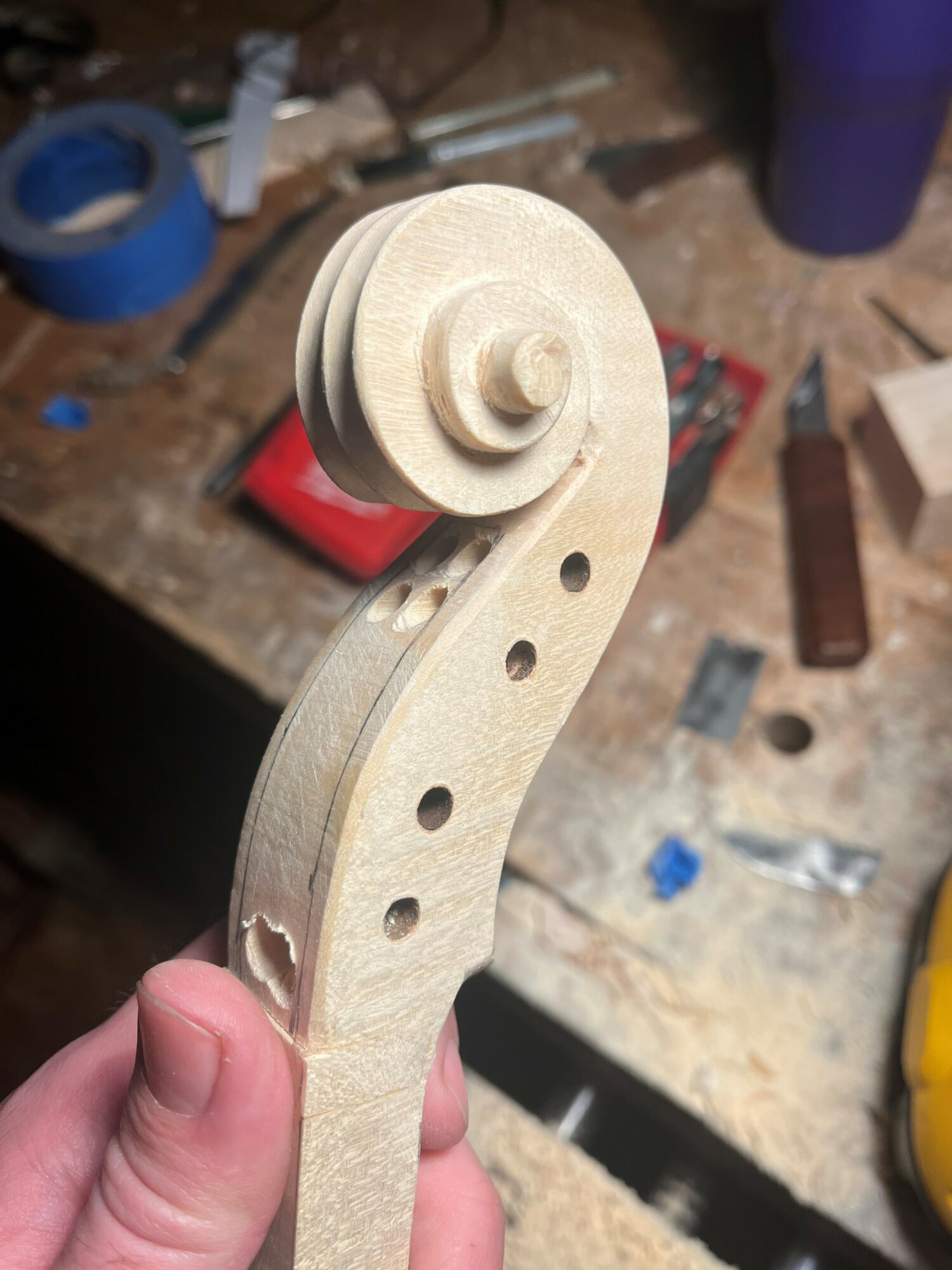 Close-up of a wooden scroll and peg on a woodworking project, held in hand, with a cluttered workbench background.