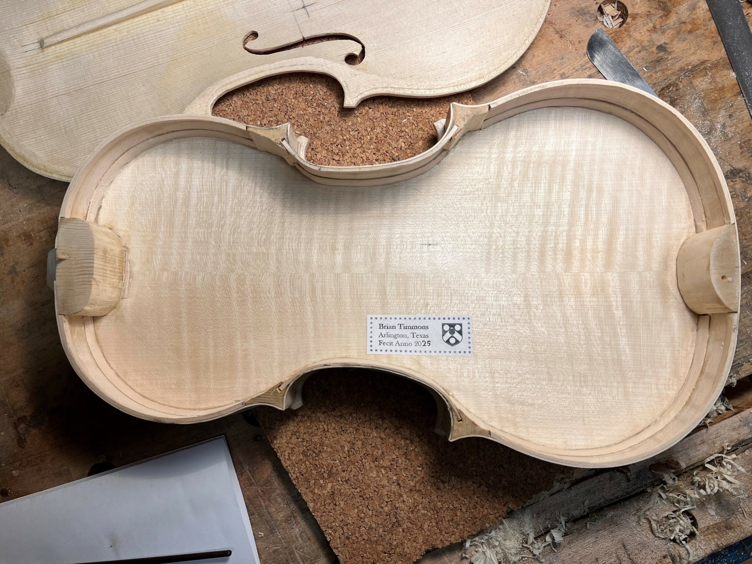 Unfinished violin case with a label inside, resting on a work surface.