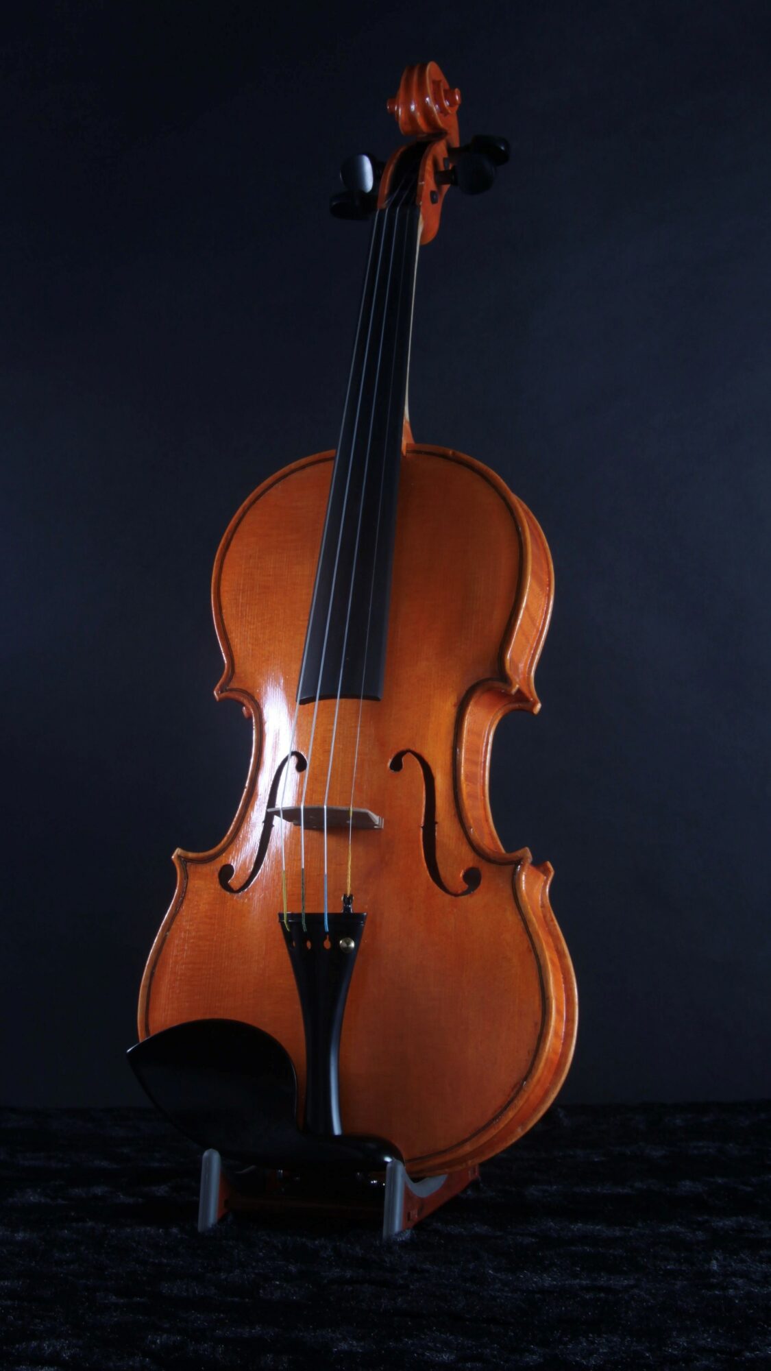 A wooden cello stands upright against a dark background, with a bow resting on top.