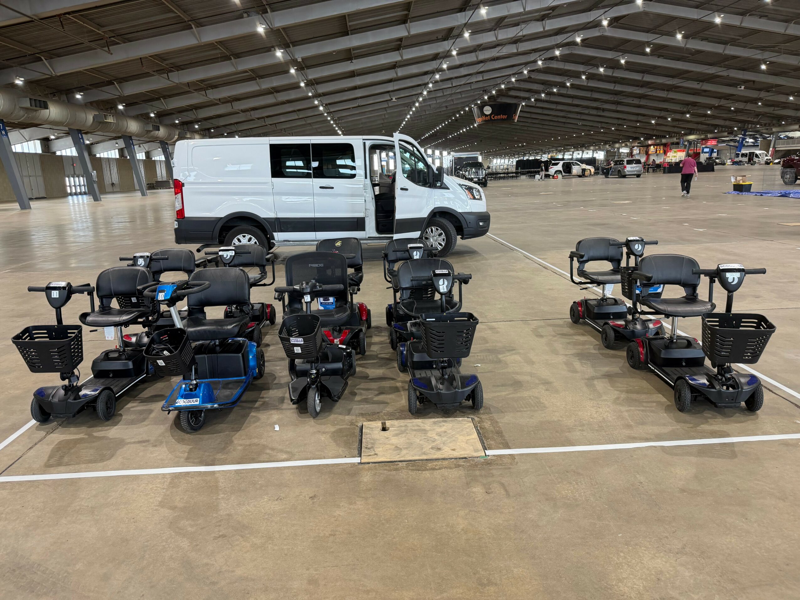 Multiple mobility scooters parked inside a large indoor space with a white van in the background.