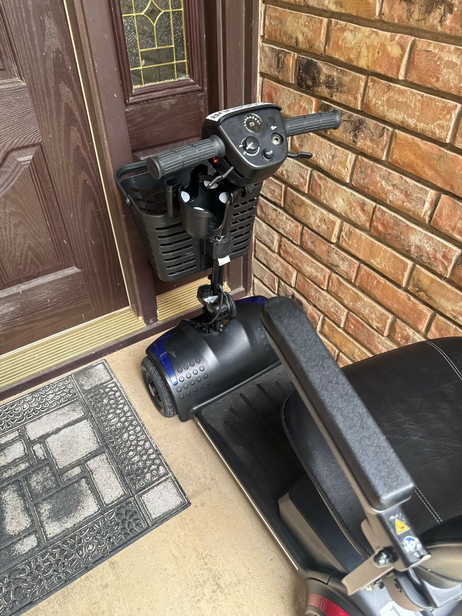 Exercise bike with black seat and handlebars, positioned next to a brick wall and a door, on a concrete floor.