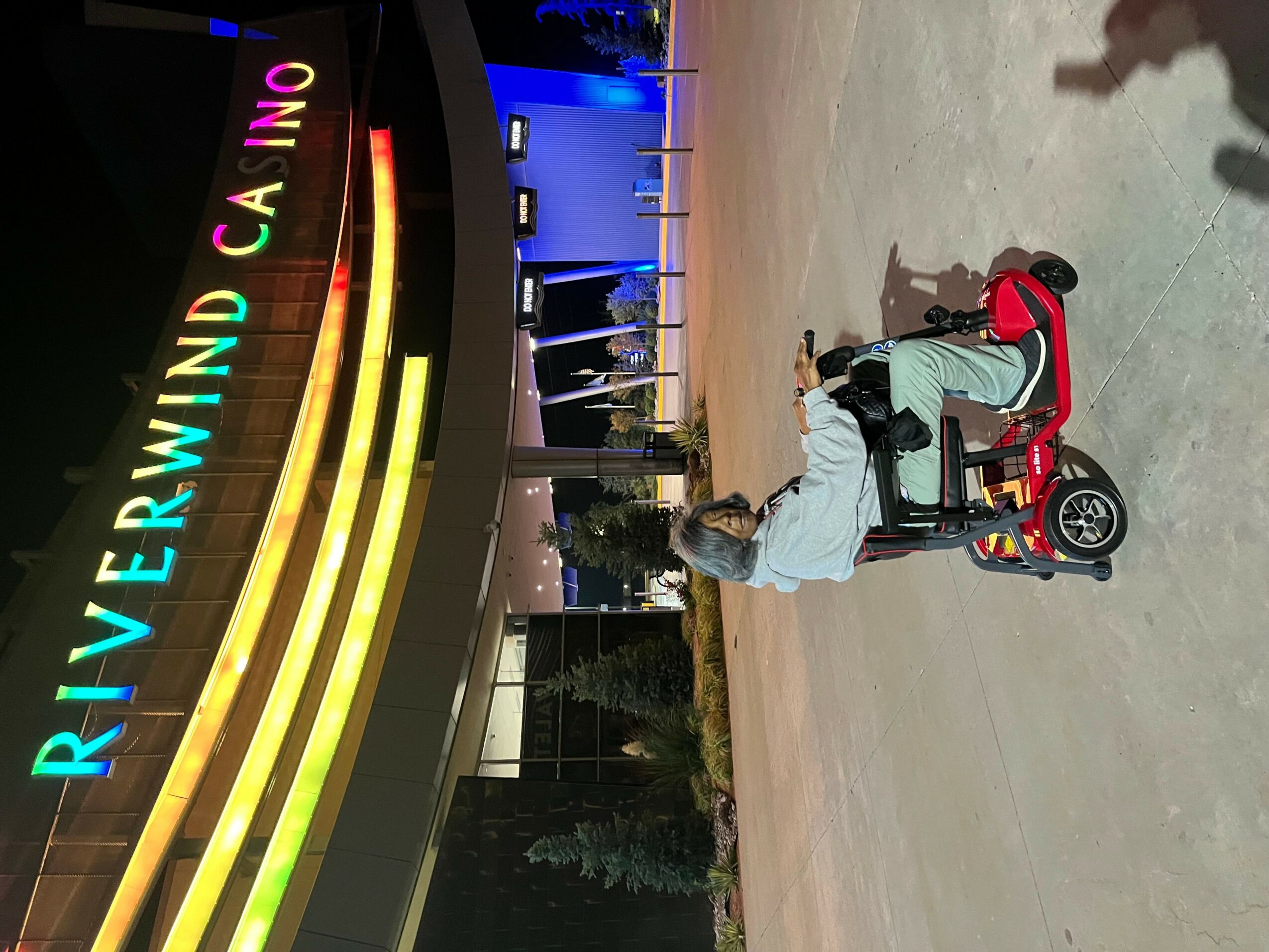 Person riding a tricycle near a brightly lit casino sign at night, with colorful lights and a dark background.