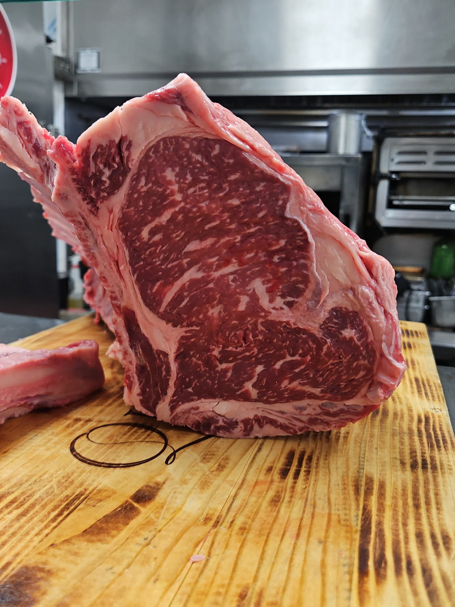 Raw marbled beef steak on a wooden cutting board in a kitchen, with a metal appliance in the background.