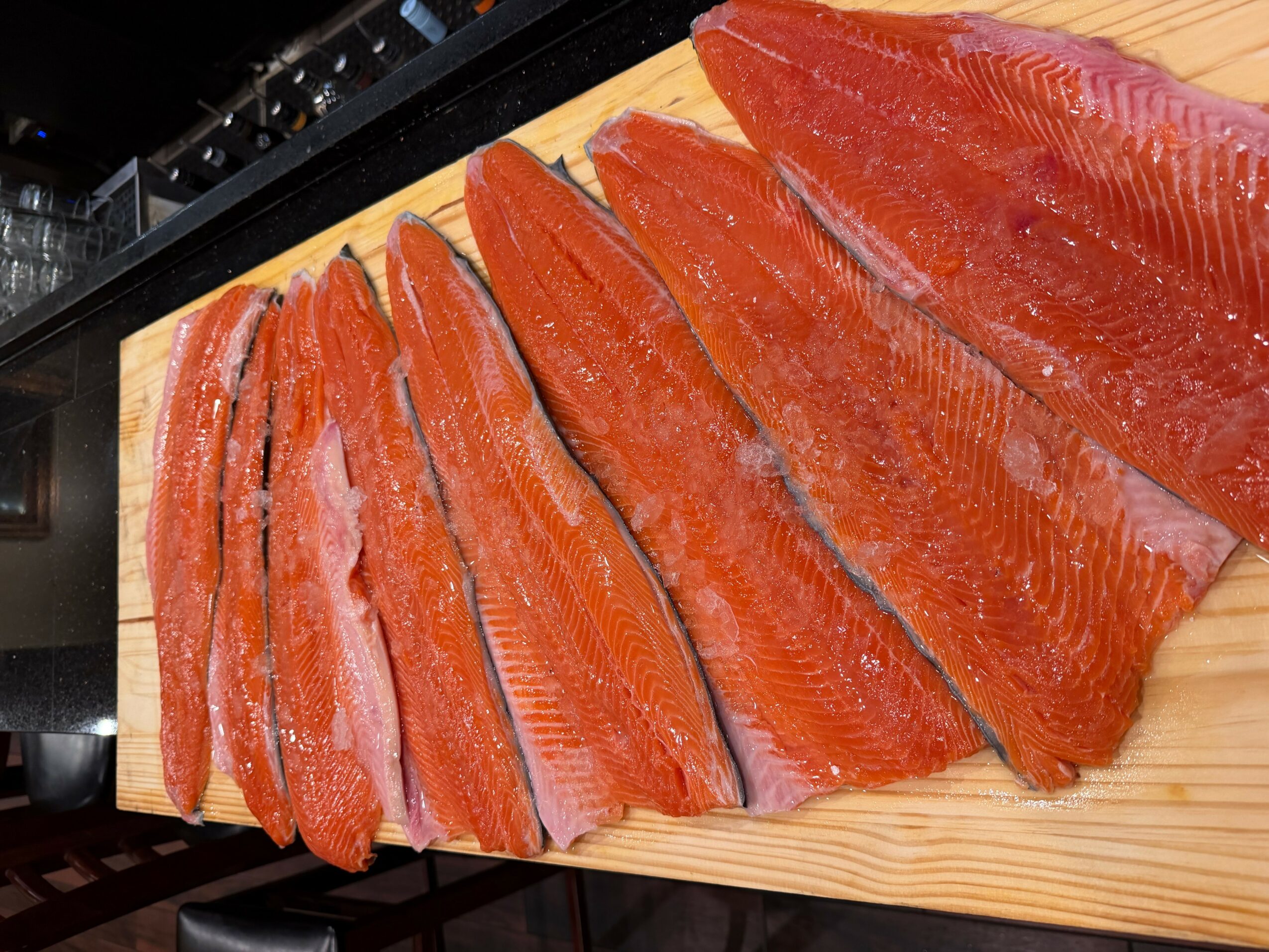 Several pieces of sliced salmon fillet on a wooden cutting board.