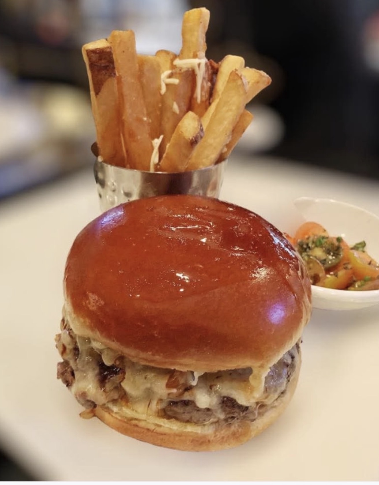 Burger with bun, patty, and toppings, French fries in a glass, side of salad, on a white plate.
