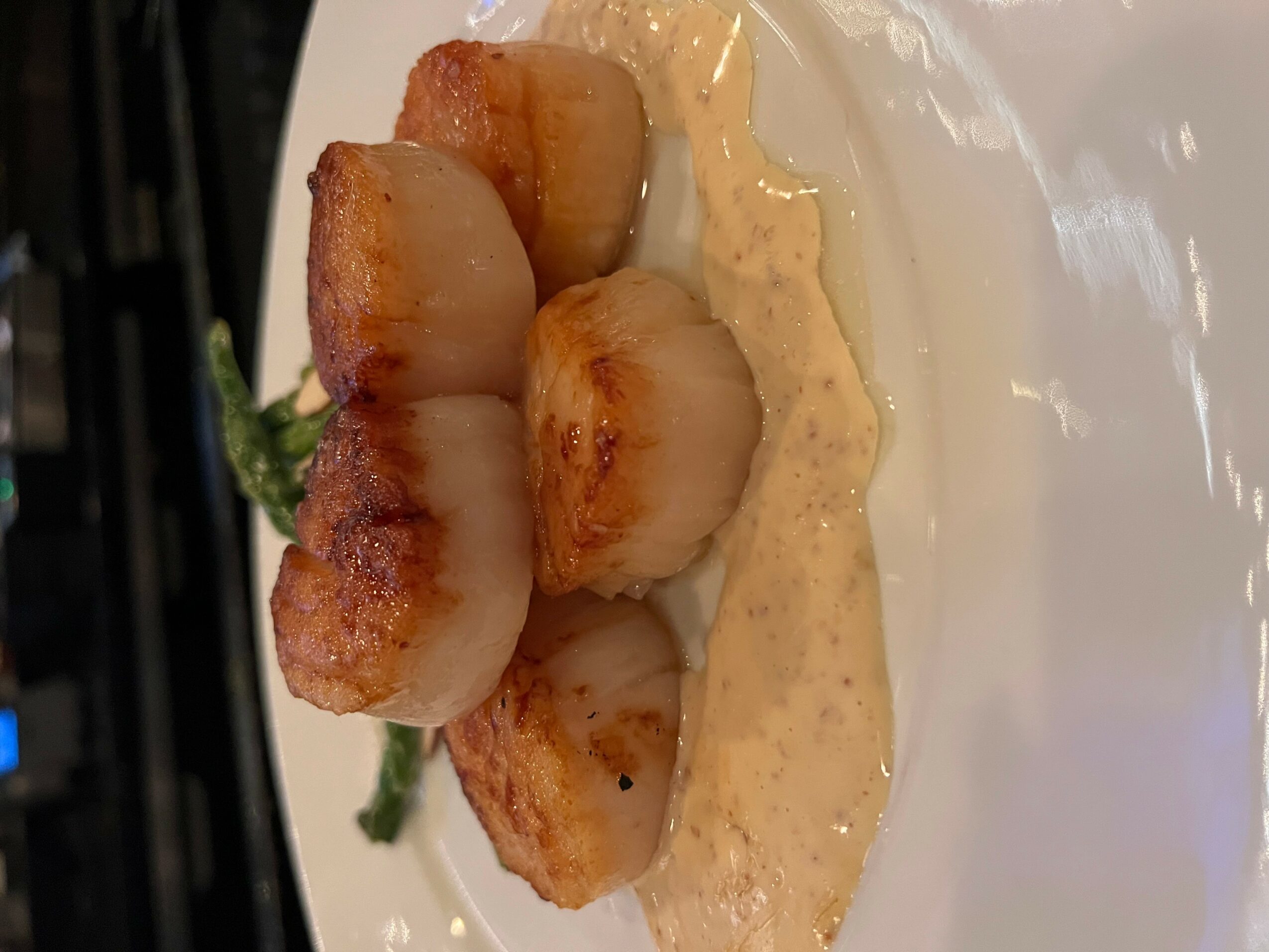 Seared scallops with a creamy sauce on a white plate, garnished with a green herb, close-up view.