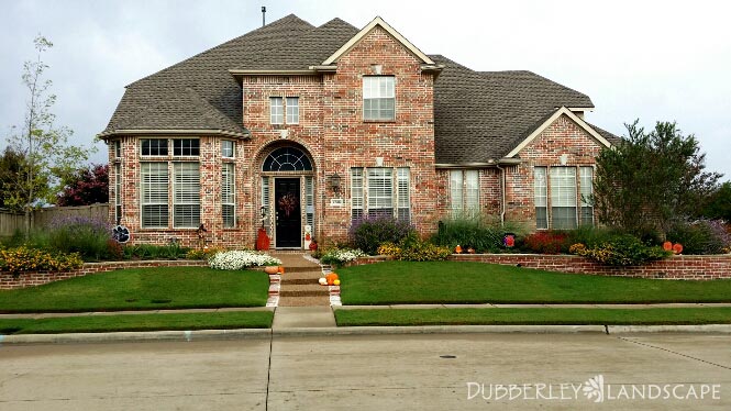 Large brick house with a front lawn, pathway, and garden, under a cloudy sky.