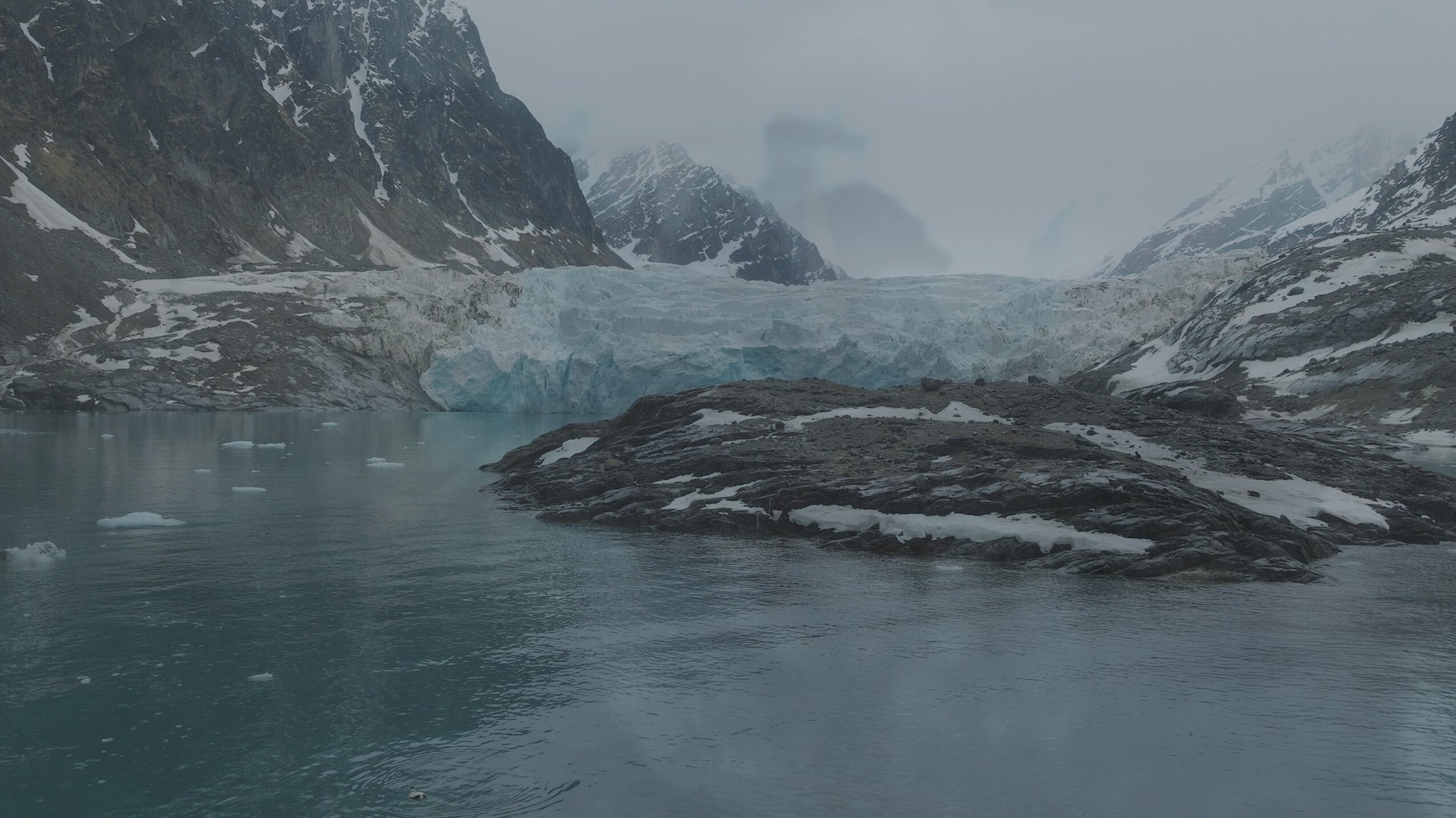 Frozen glacier in a mountain landscape with icy water and snow-covered peaks.