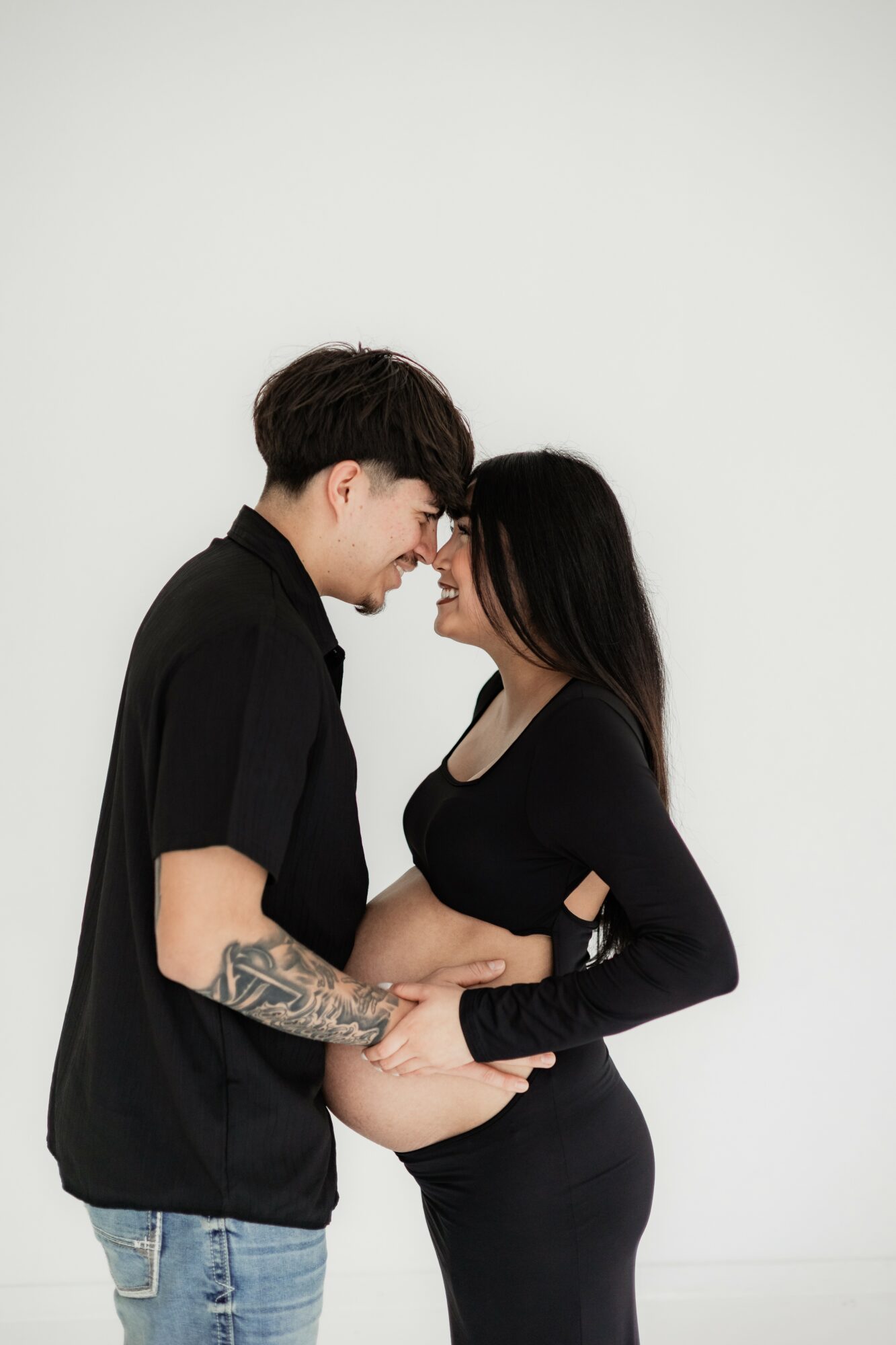A man and woman face each other closely, holding hands, against a plain white background.