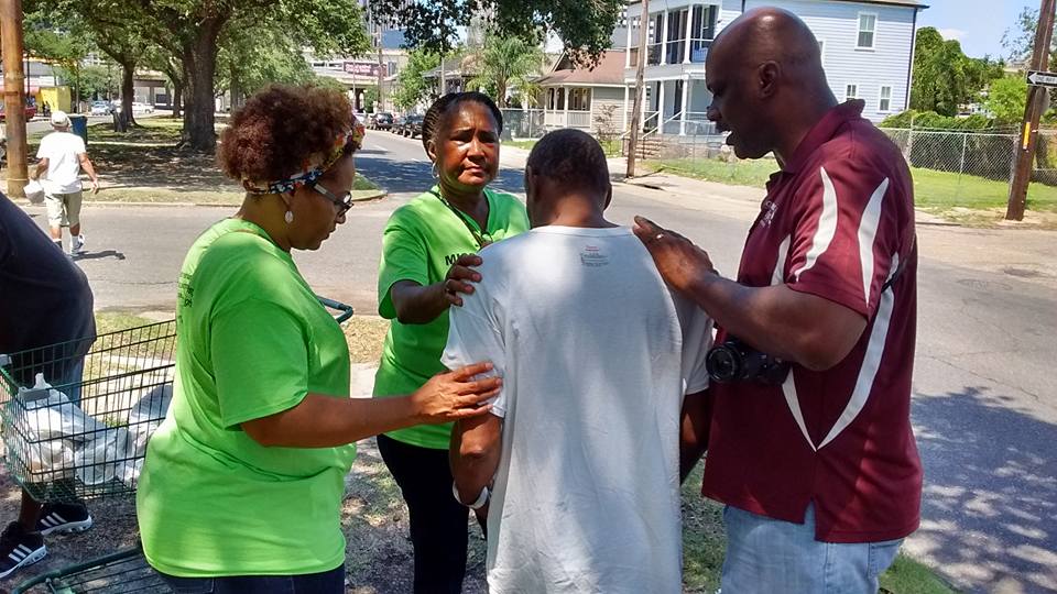 Four people standing outdoors, two women and two men, engaged in conversation on a sunny day.