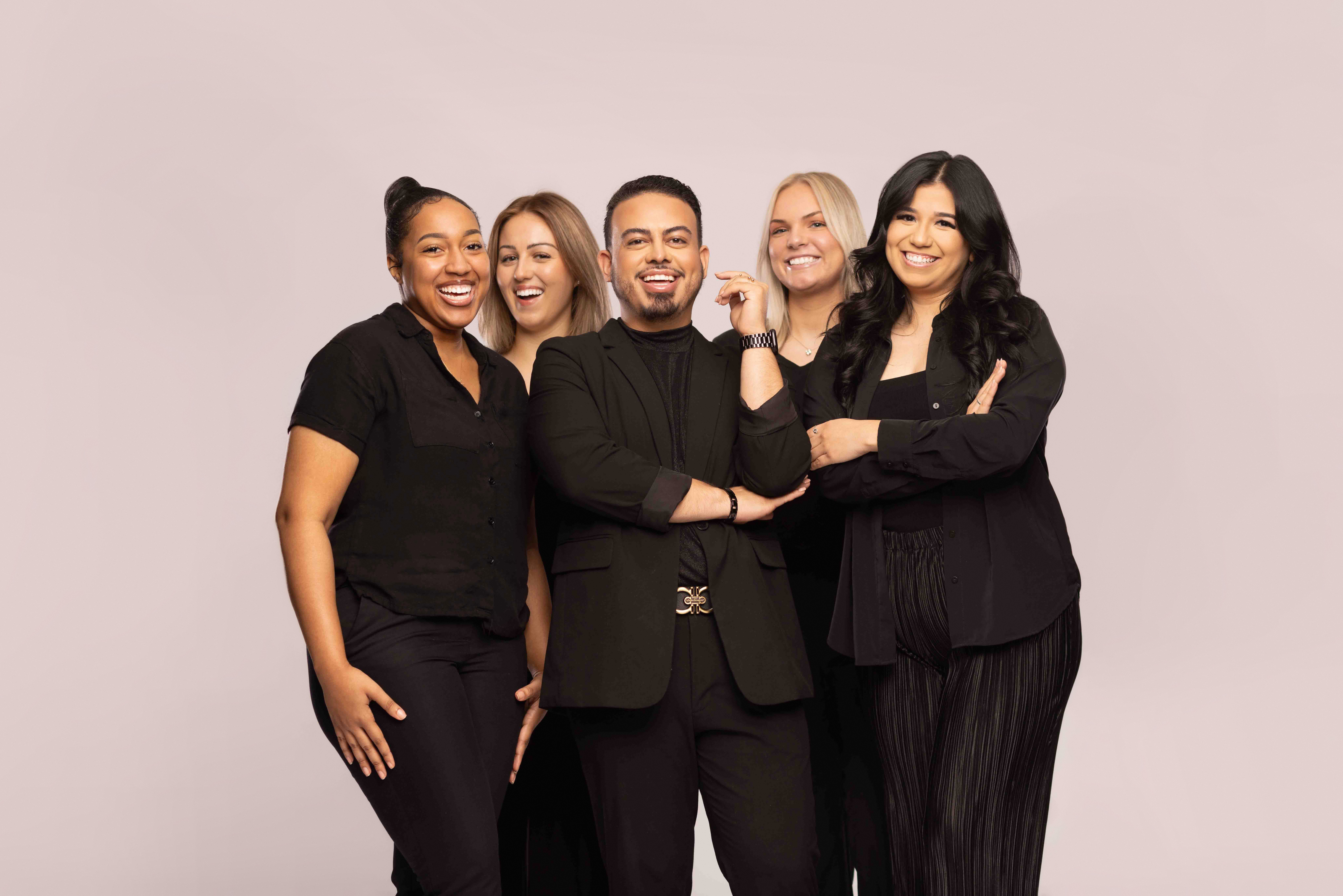 Five diverse people smiling and standing together against a plain background.
