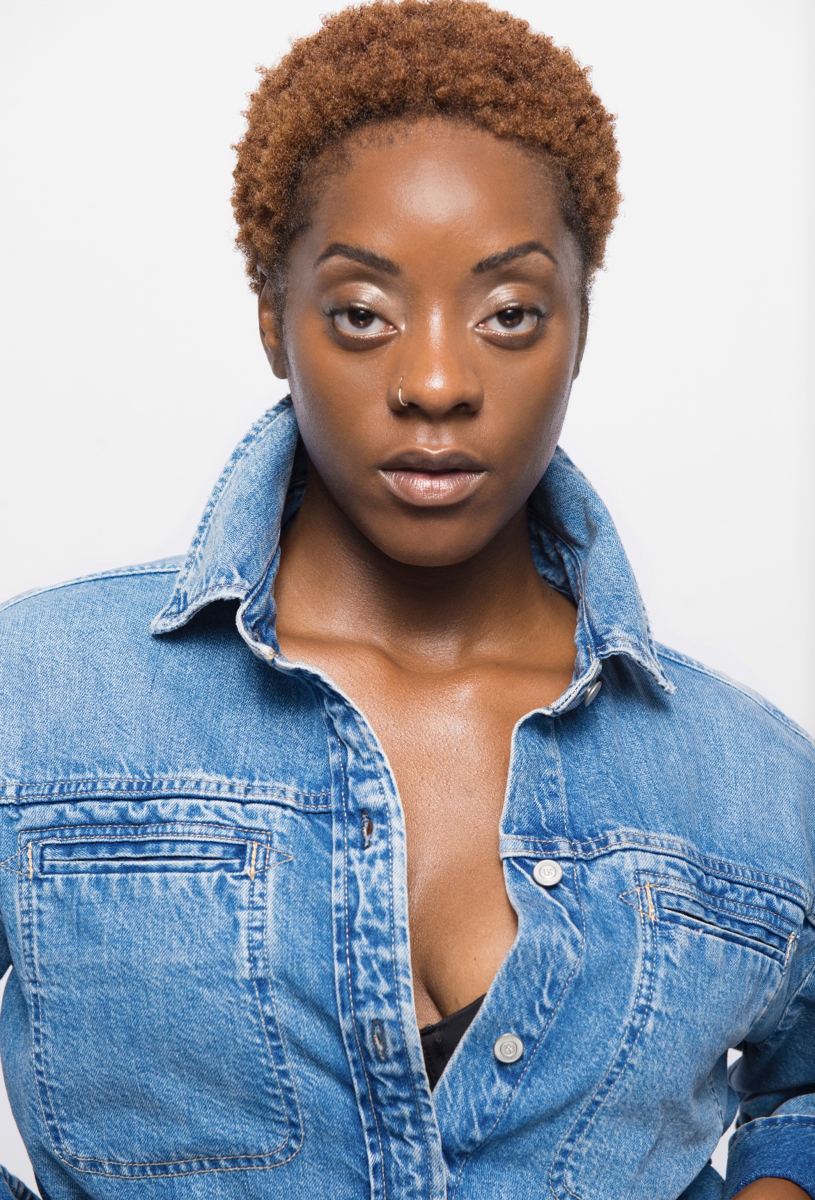 Portrait of a woman with short curly hair wearing a denim jacket, looking directly at the camera.