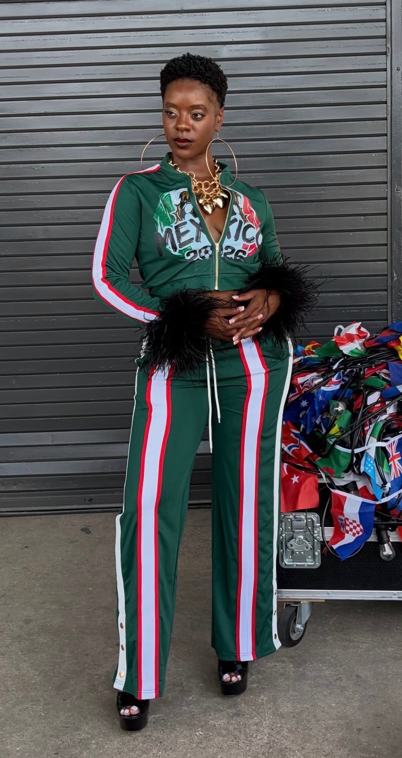 Woman in green tracksuit with red, white, and green stripes, standing outdoors with a shopping cart filled with colorful items.