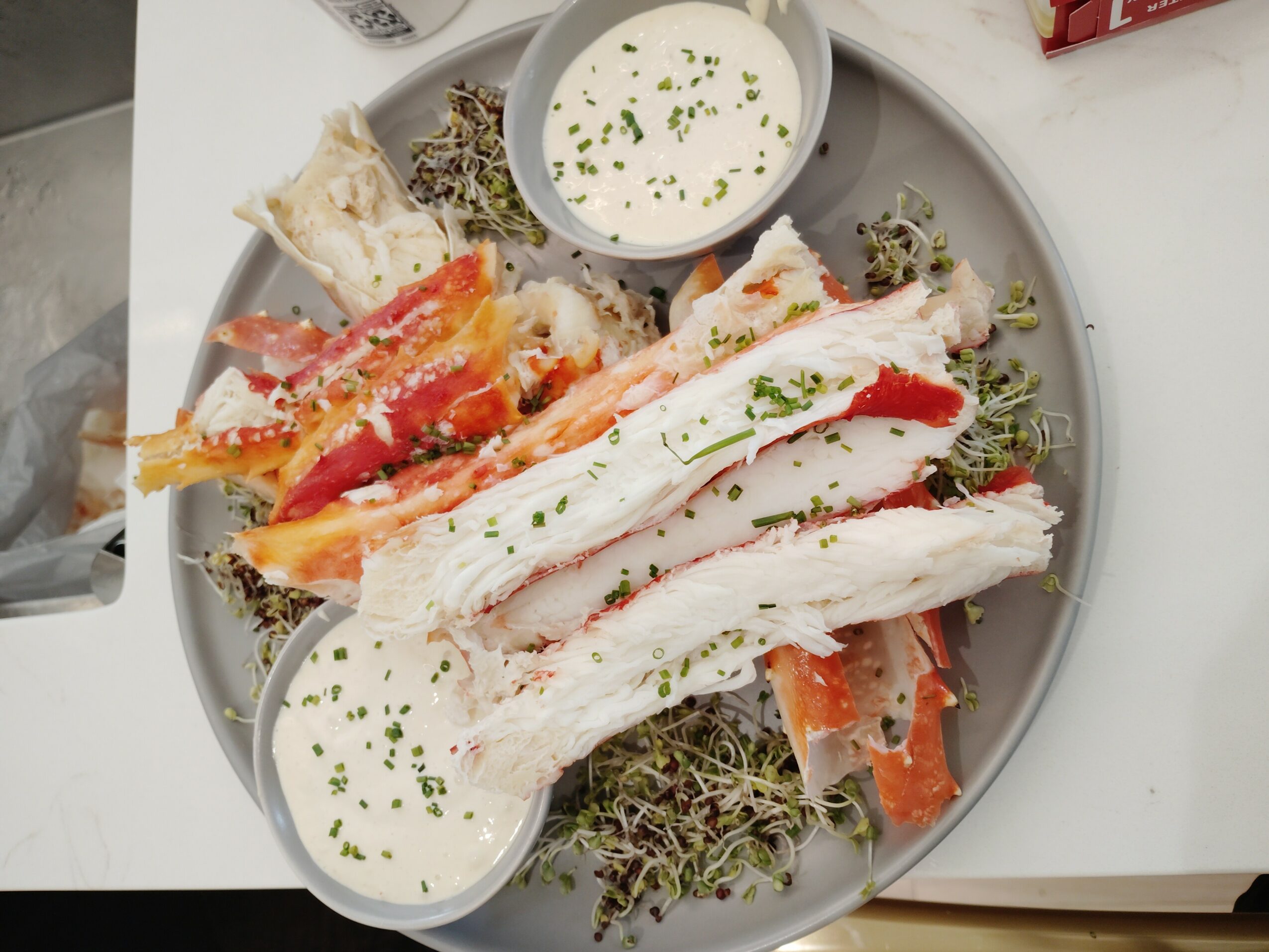 Plate with crab legs, vegetables, and two bowls of white dipping sauce garnished with herbs.