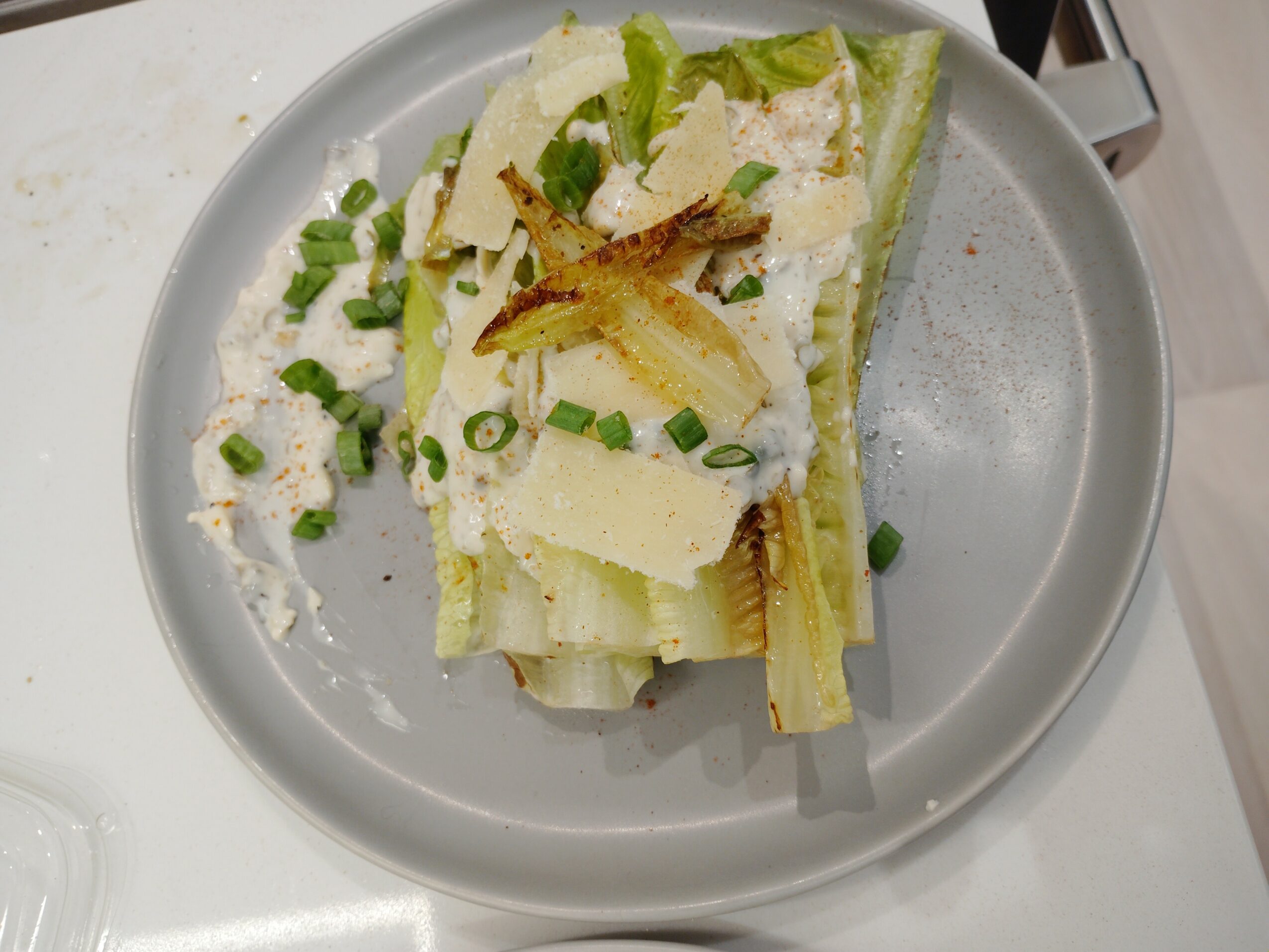 A layered dish with lettuce, cheese, and fried toppings on a gray plate, garnished with chopped green onions.
