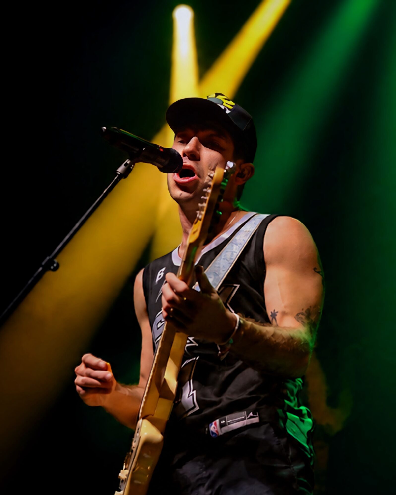 Male musician singing into microphone and playing guitar on stage with green and yellow lighting