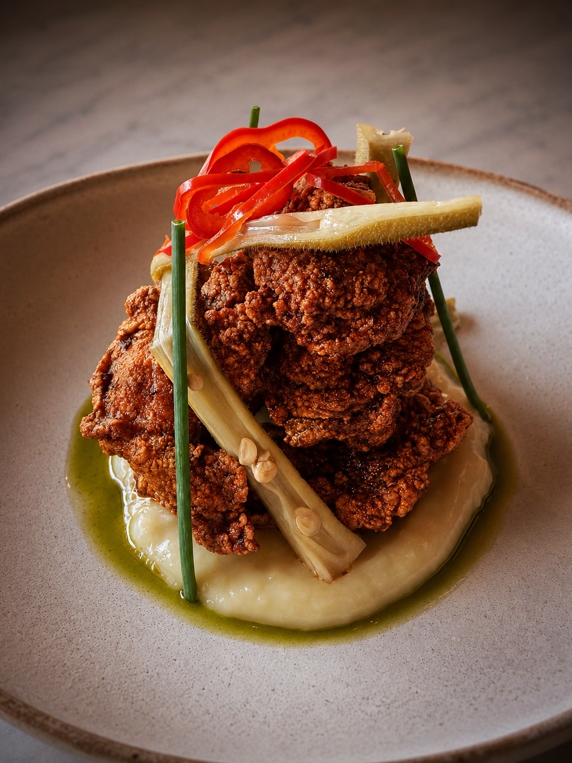 Fried chicken on mashed potatoes with green beans and red pepper slices, garnished with lemon wedge, on a white plate.
