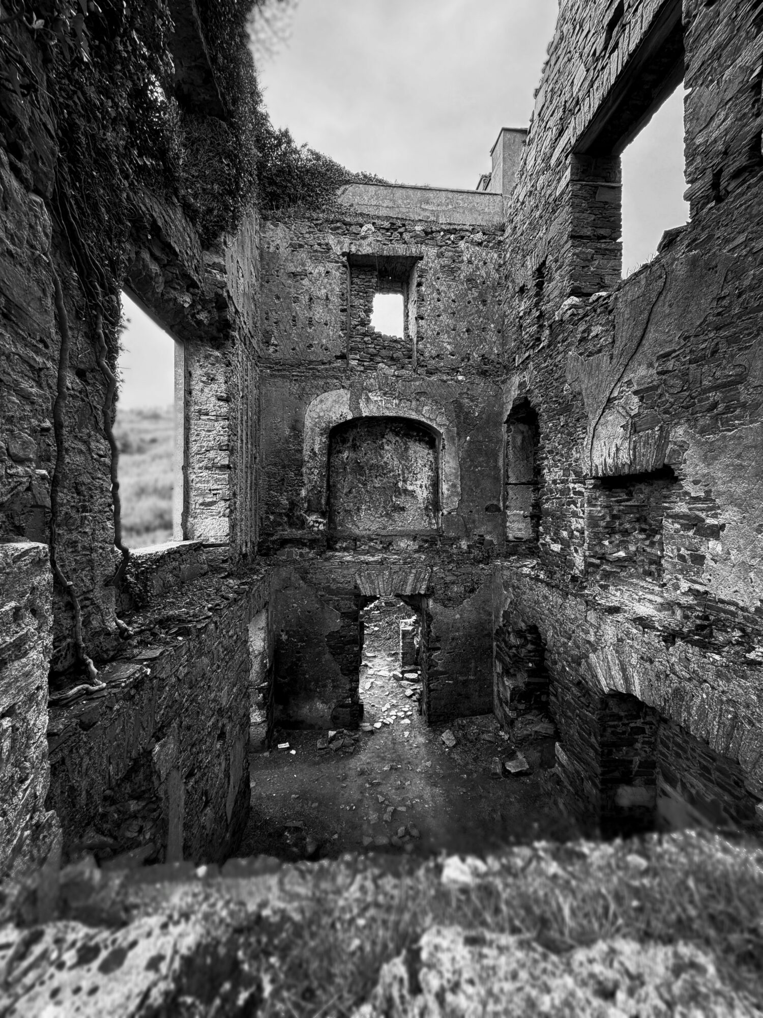 Ruins of an old stone building with multiple archways and windows, in black and white.