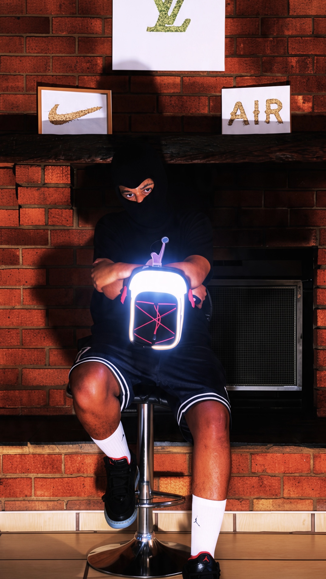 Person sitting on a stool with a glowing electronic device, in front of a brick wall with Nike and Air logos.