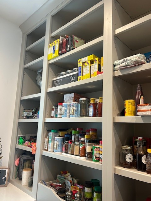 Tall gray pantry shelf filled with jars, boxes, and containers of food and spices, with some items on the floor.