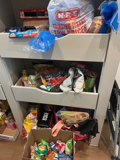 Shelves with snacks, drinks, and grocery items in a room, including chips, bottled drinks, and packaged foods.