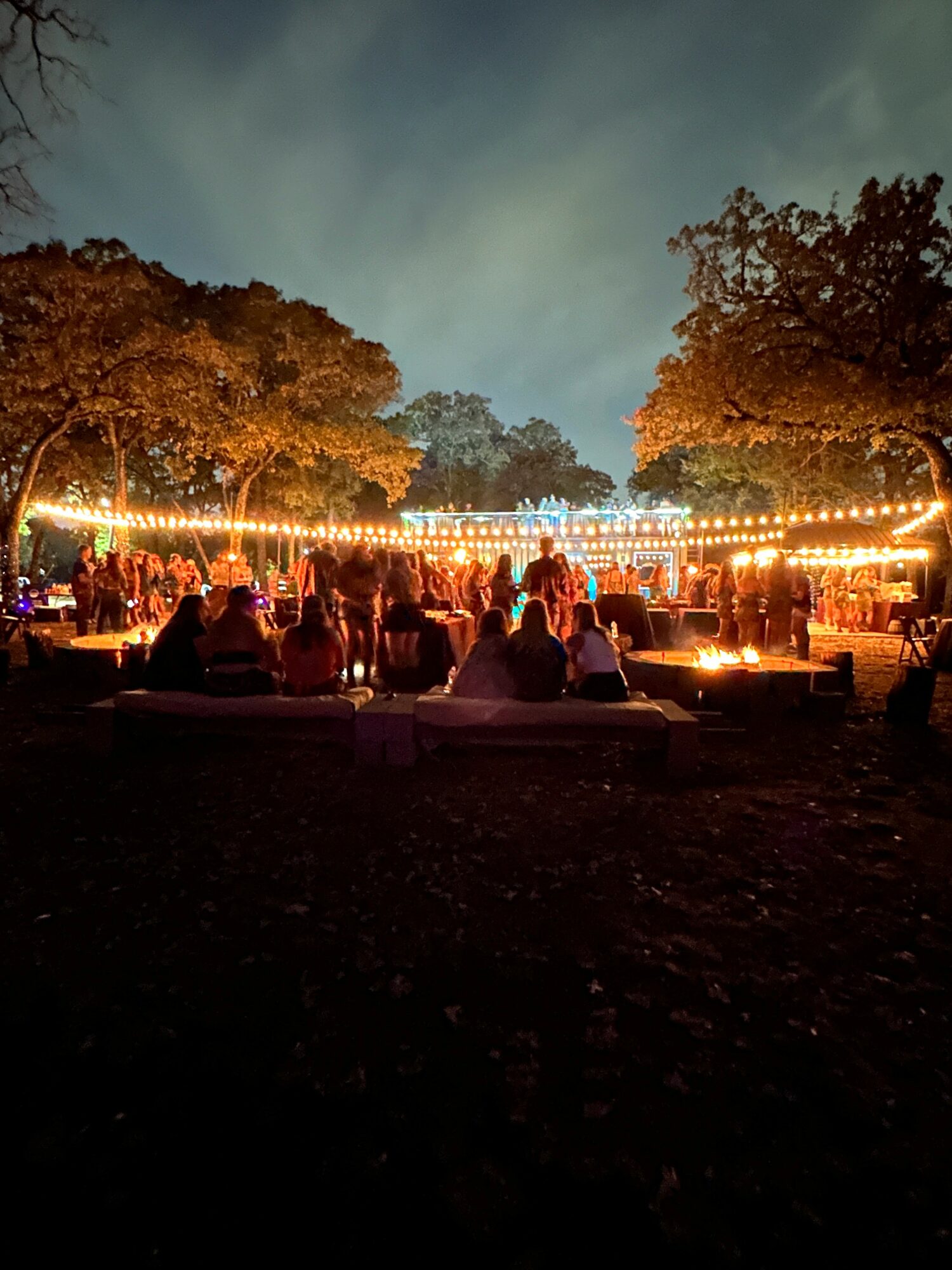 People gather outdoors at night under string lights, with trees and a dark sky in the background.
