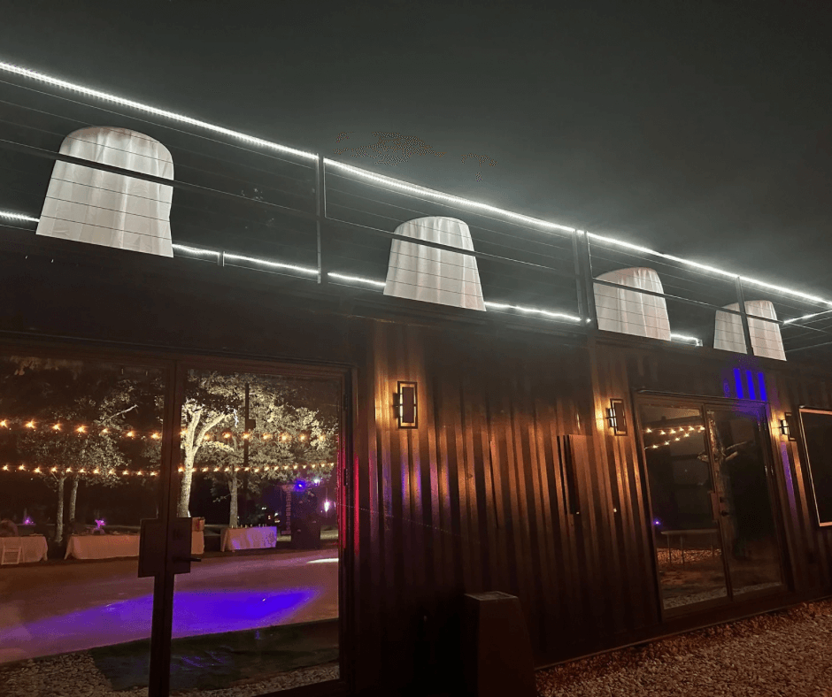 Night scene of a building with illuminated rooftop structures and a glass window reflecting trees and lights outside.
