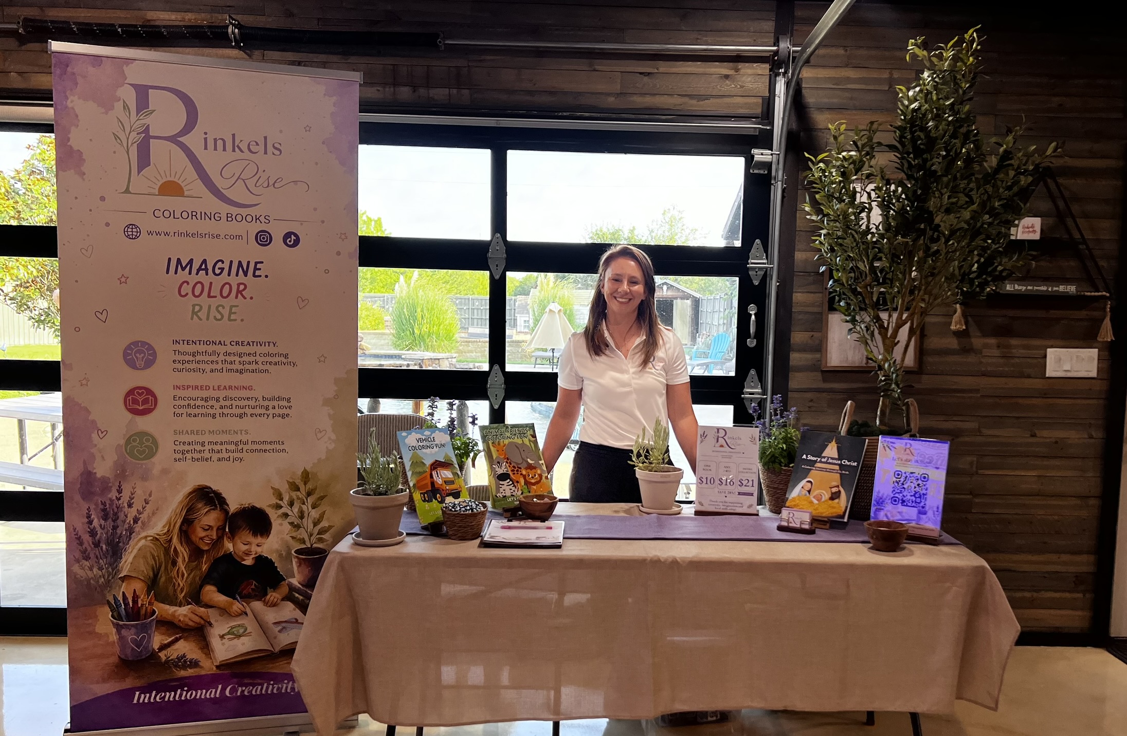 Woman standing behind a table with promotional materials inside a building with large windows and wooden walls.
