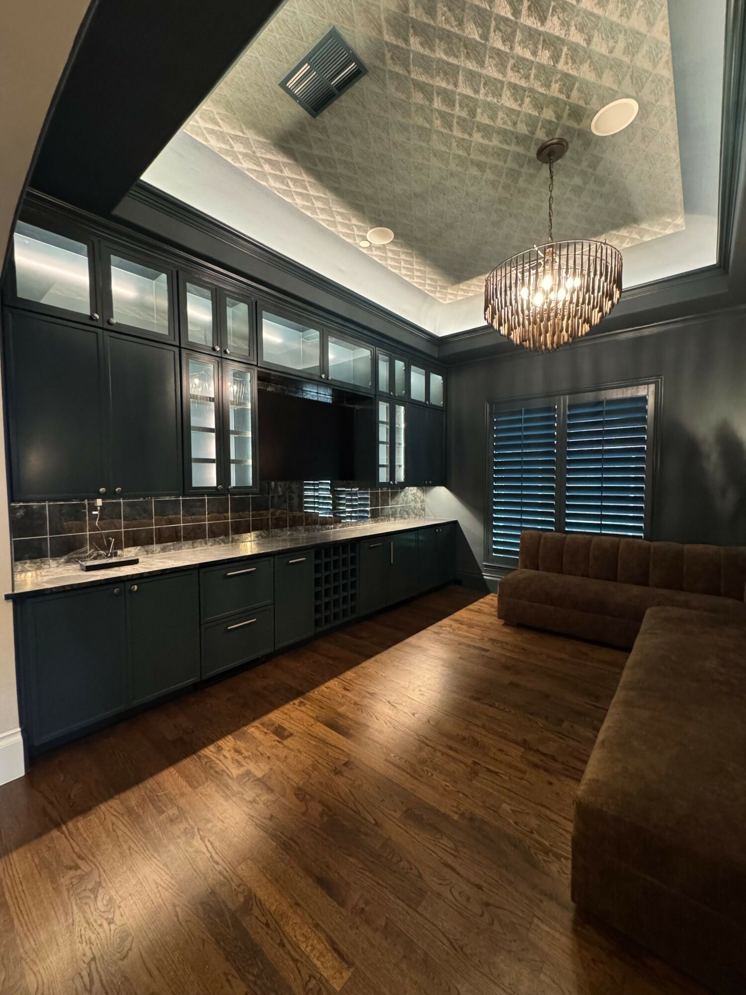 View of a modern kitchen with black cabinets, a brick backsplash, and a wooden floor, seen from a tilted angle.